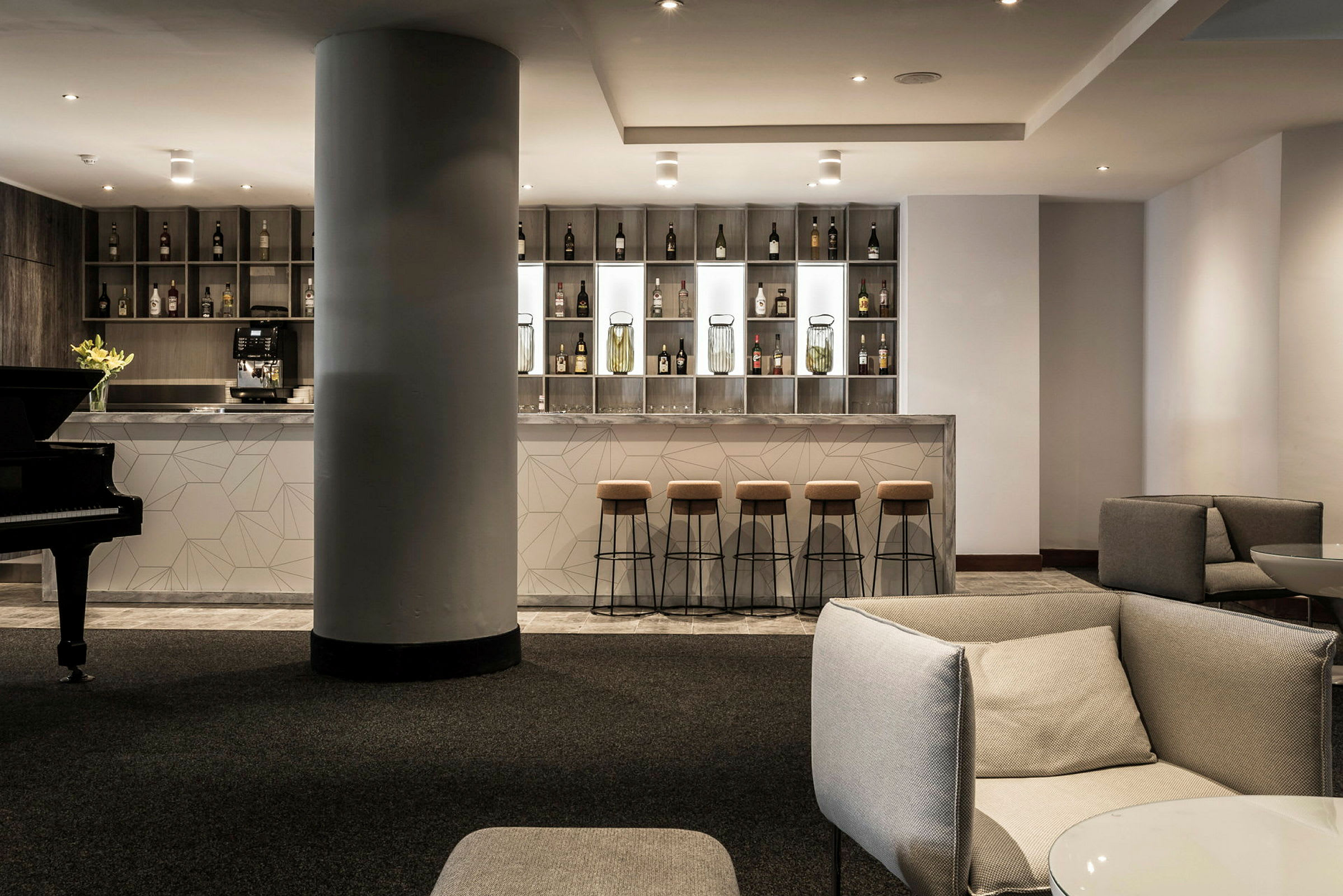En stilren hotellbar med höga barstolar och en modern design. Till vänster syns ett piano. (AI-genererad text)