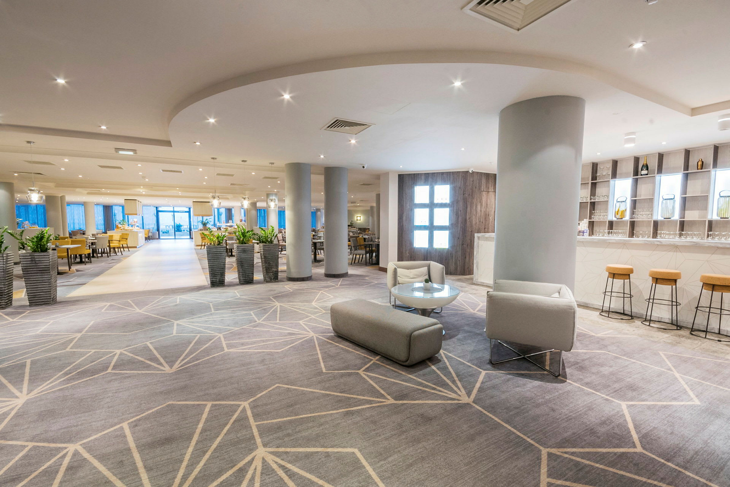 En ljus och modern hotellobby med sittmöbler och flera växter i krukor. (AI-genererad text)