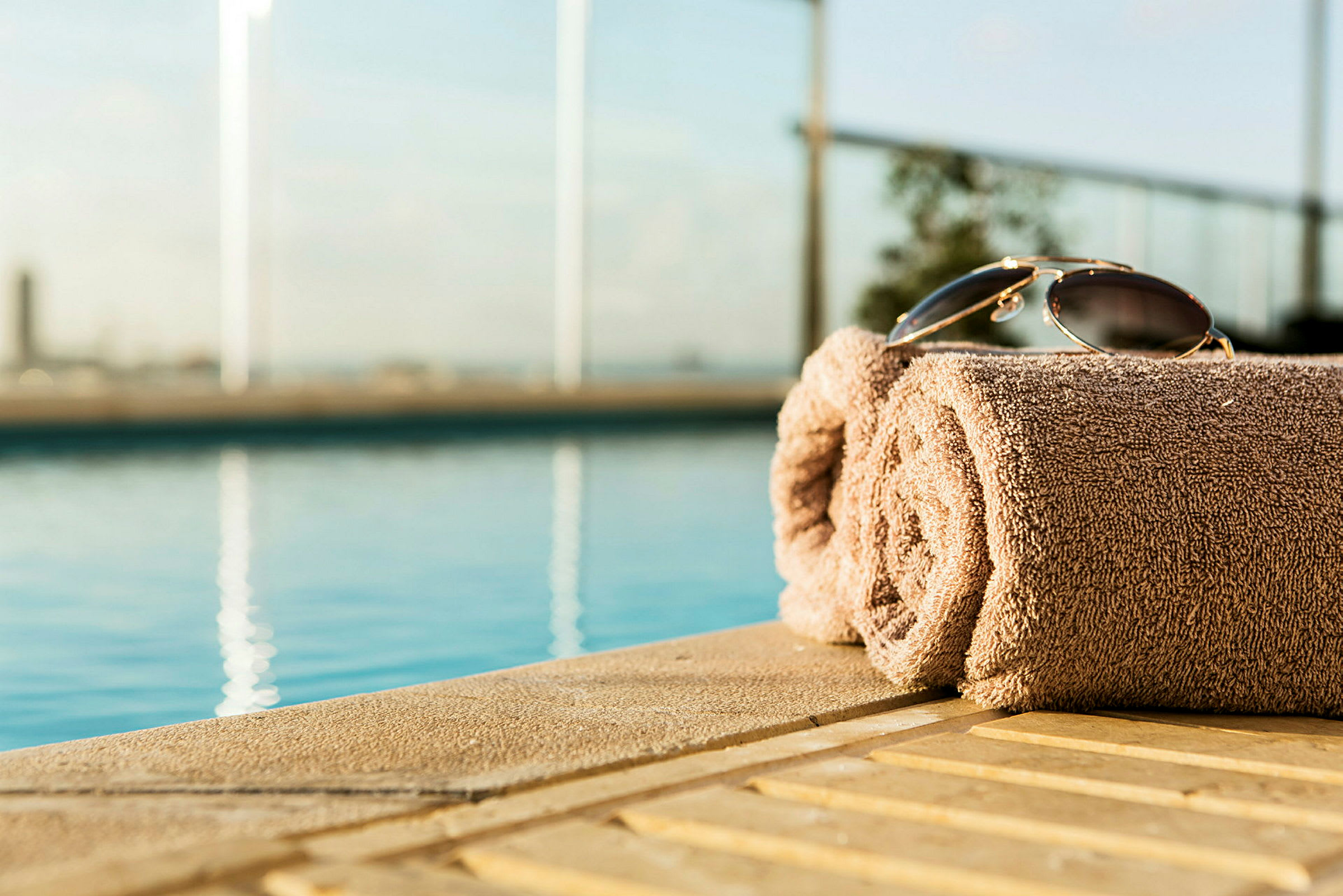 En hoprullad handduk med ett par solglasögon placerade ovanpå vid kanten av en pool. (AI-genererad text)