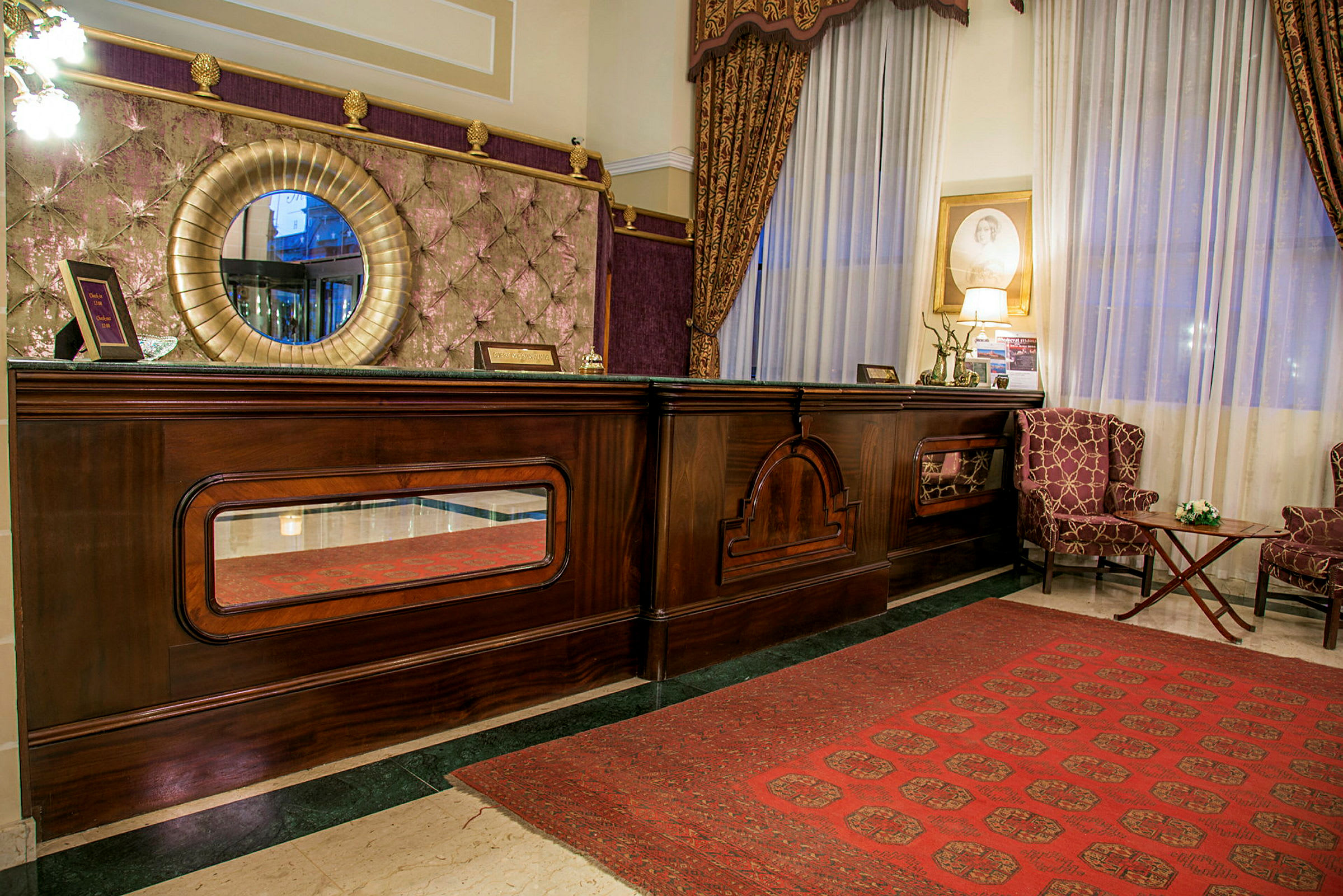 Bild av en hotellreception med en elegant trädisk, rund spegel och två fåtöljer framför ett stort fönster. (AI-genererad text)