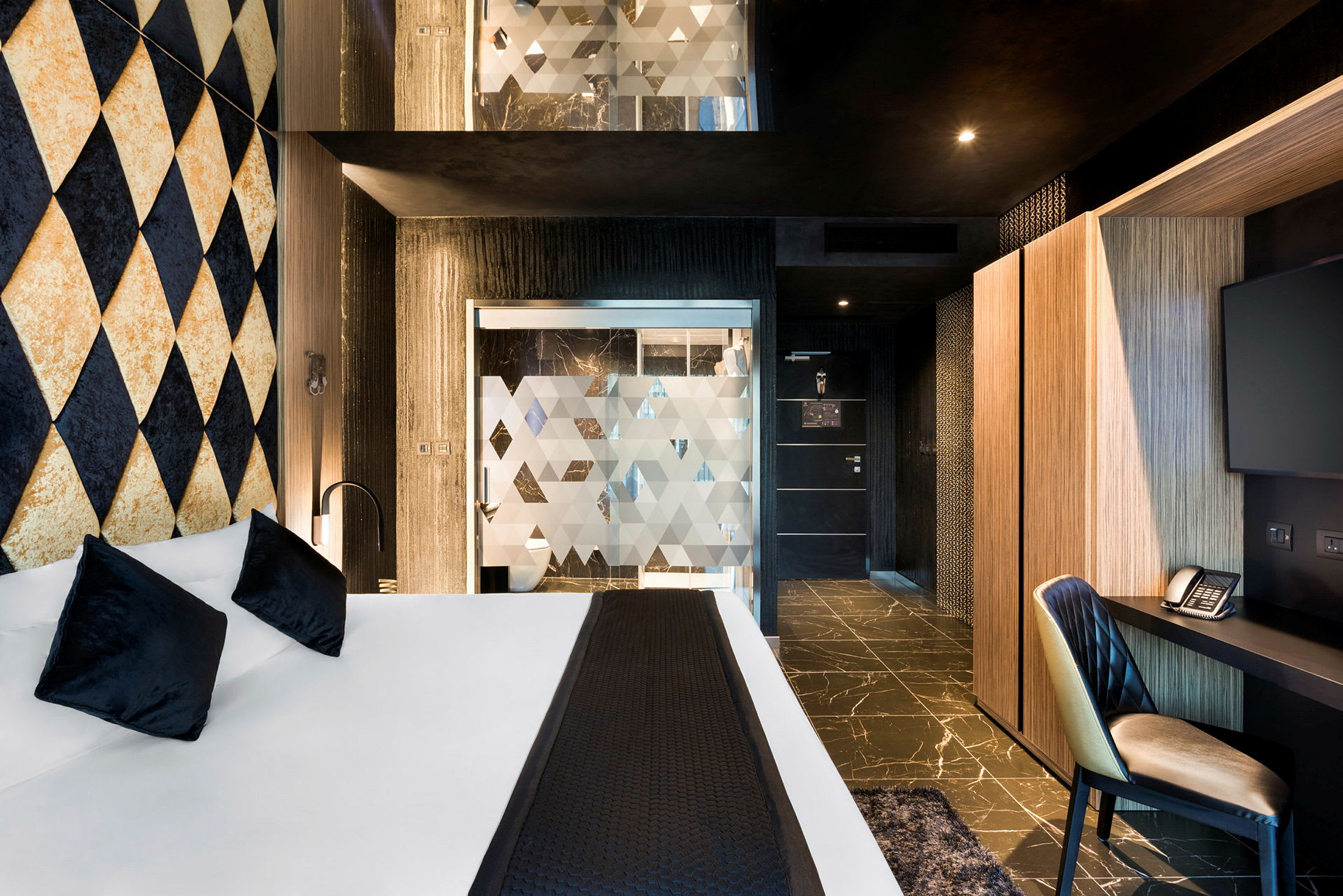 Hotellrum med modernt designad inredning, säng med vita lakan och svarta kuddar, samt arbetsyta med stol, skrivbord och TV. (AI-genererad text)