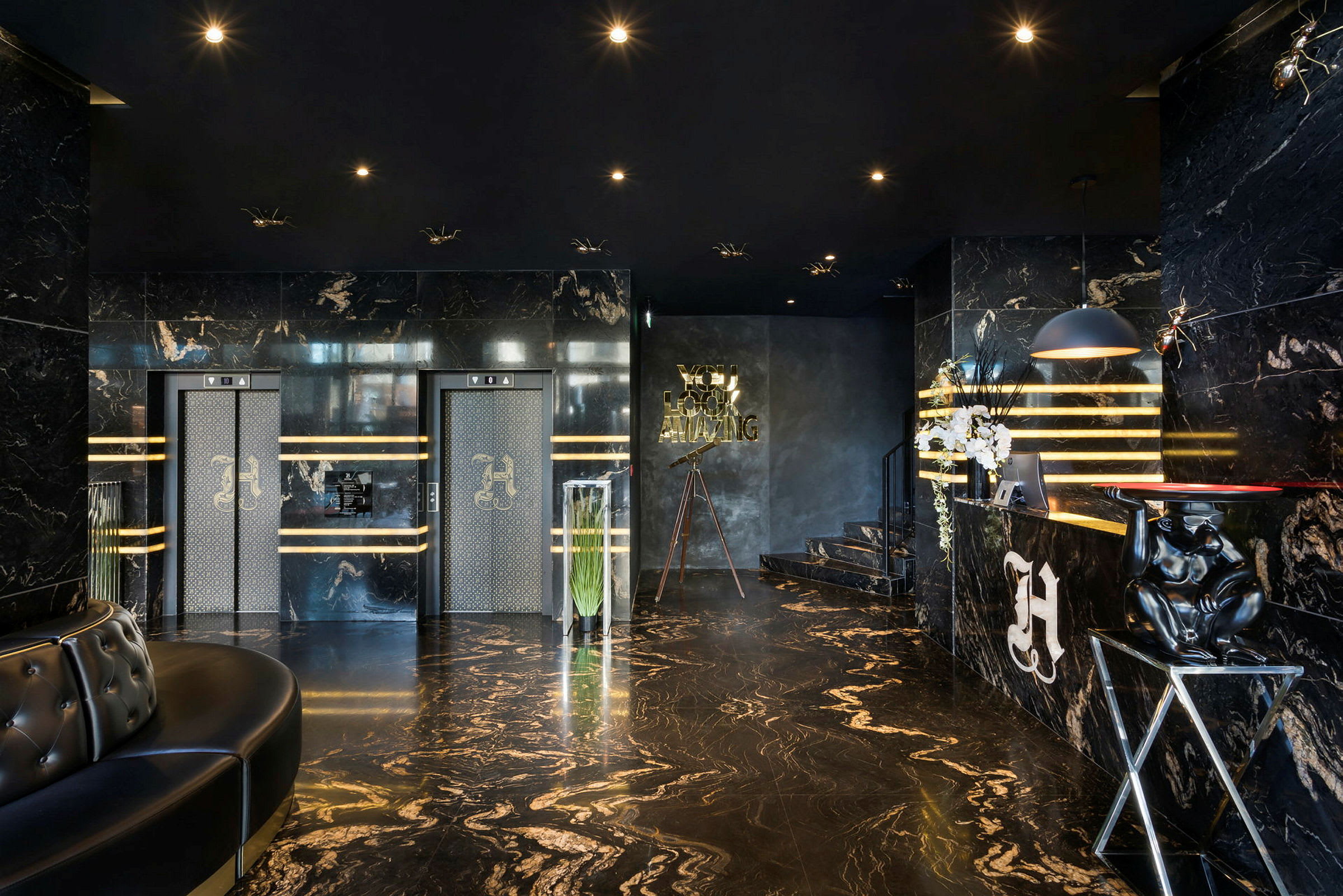 Ett elegant hotellfoajé med marmorgolv och väggar, två hissar med dekorerade dörrar, och en reception med lyxig inredning. (AI-genererad text)