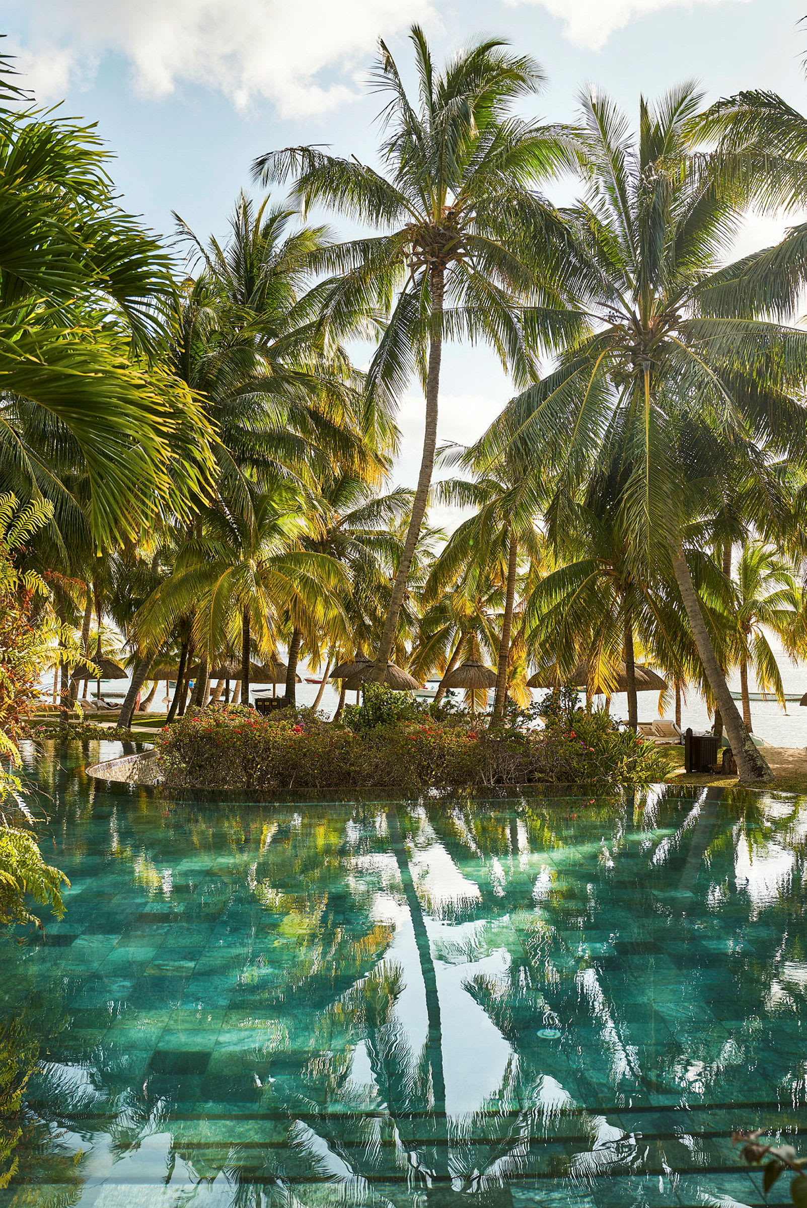 En pool omgiven av frodig vegetation med palmer och utsikt mot havet. (AI-genererad text)