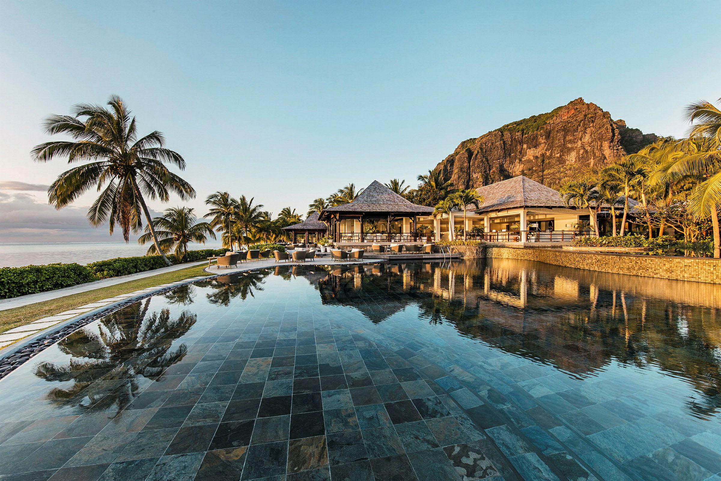 En infinitypool med utsikt över palmer, en lyxig resort och en bergsformation i bakgrunden. (AI-genererad text)