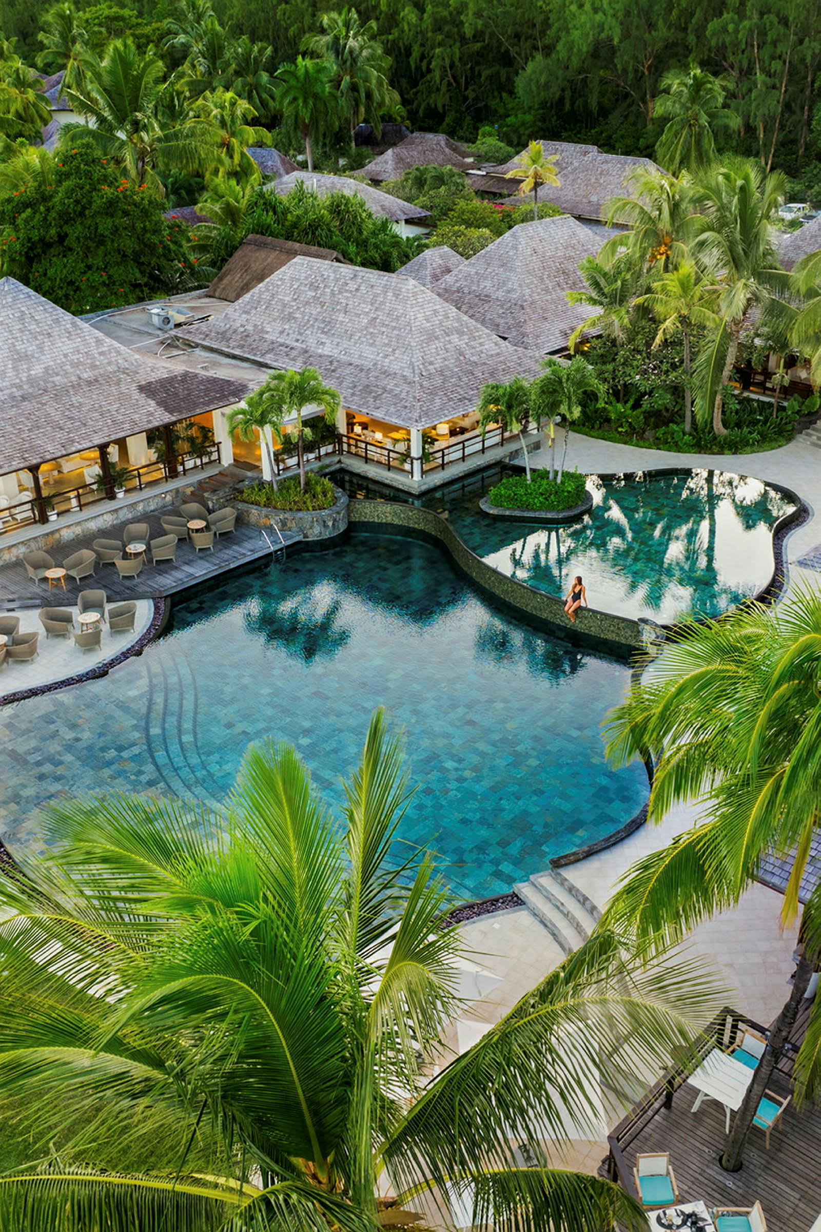 En pool vid en resort omgiven av tropiska växter och palmer. (AI-genererad text)