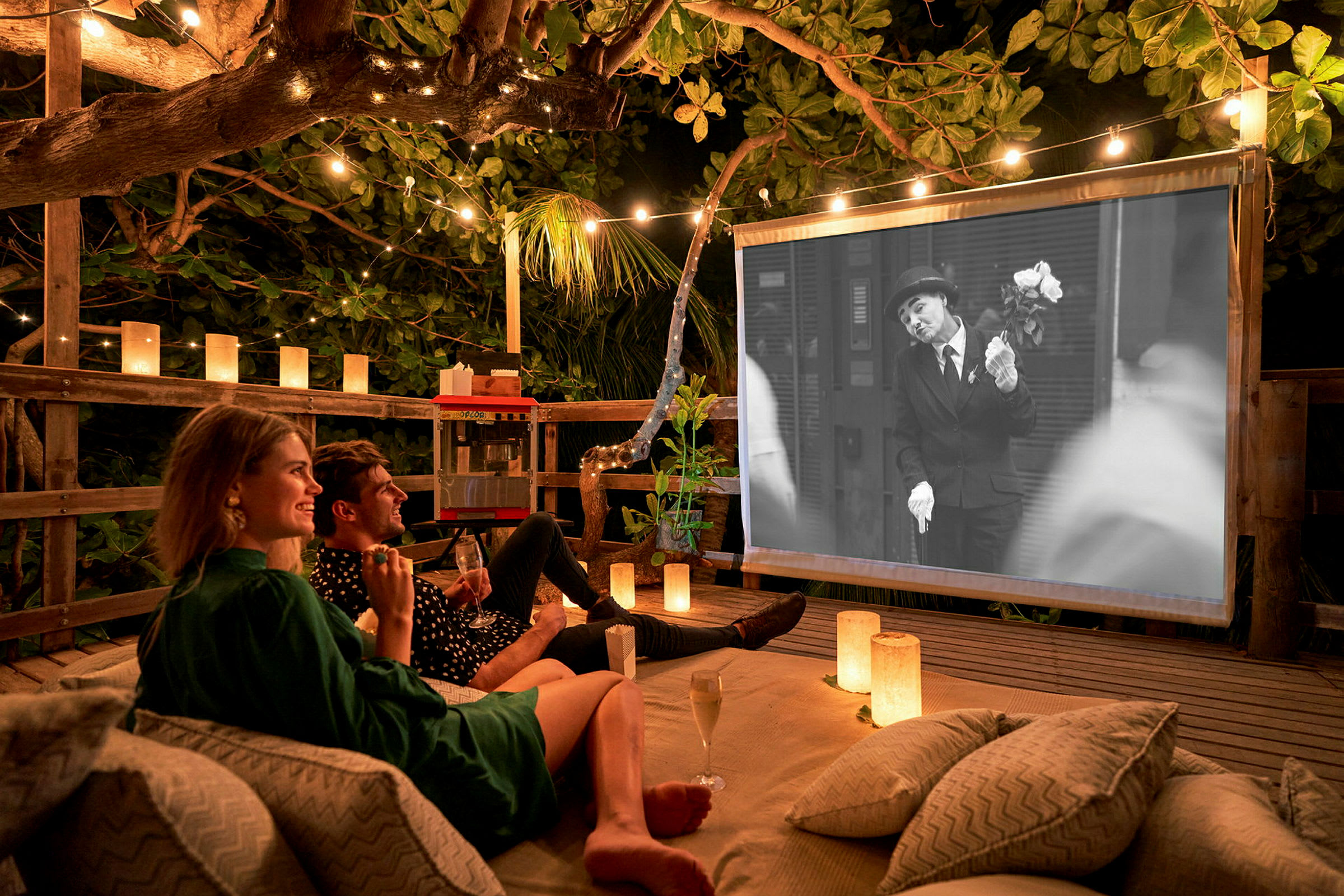 En utomhusbio med en film som visas på en duk, omgivna av belysning och träd. (AI-genererad text)