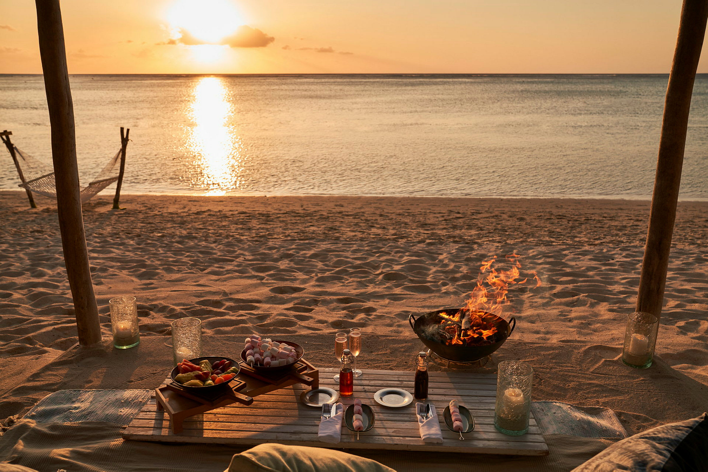 Dukat bord på en strand med en solnedgång i bakgrunden och en eld i en eldstad. (AI-genererad text)