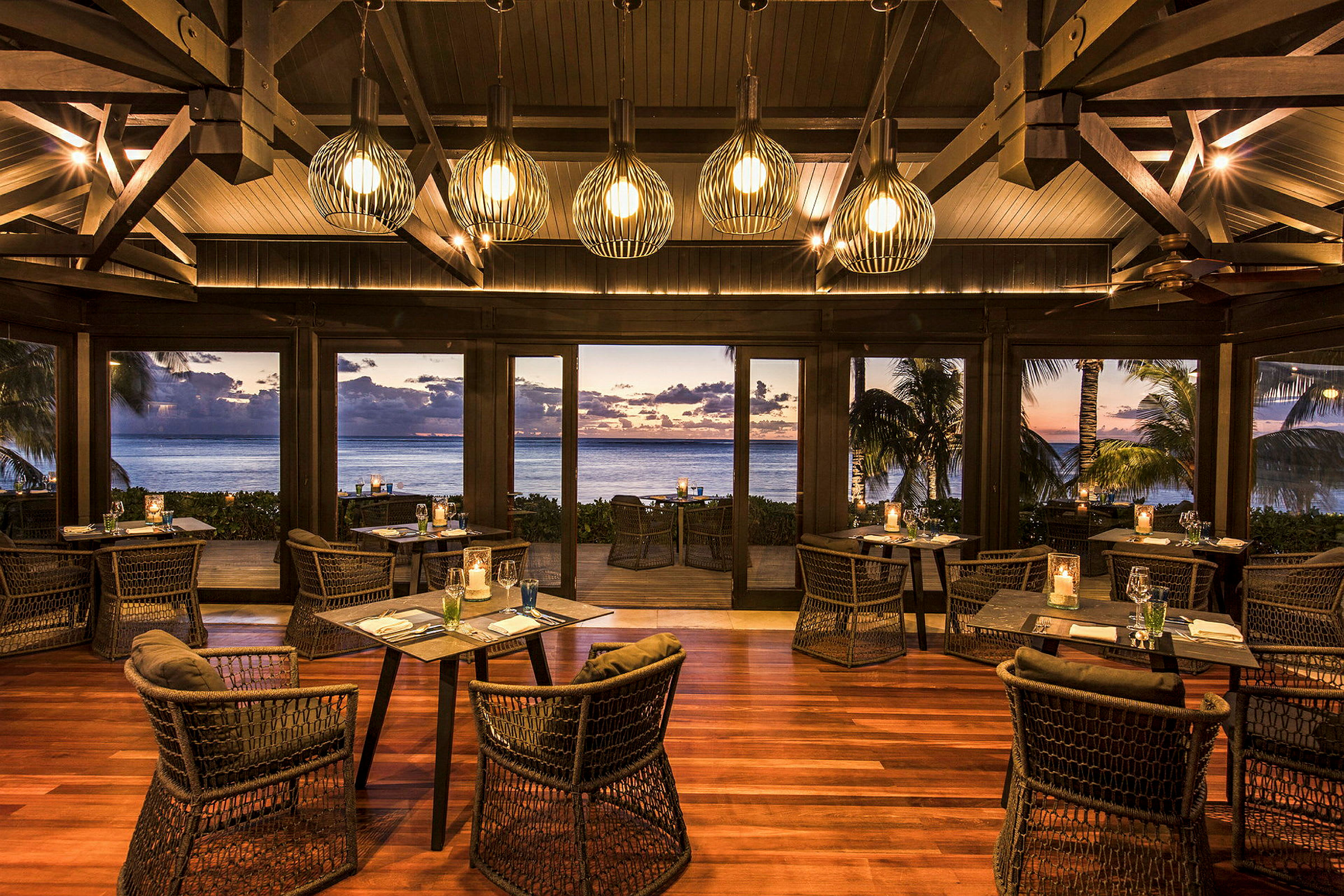 En elegant restaurang med träinredning och moderna stolar. Fönstren erbjuder en utsikt över havet med en solnedgång i fjärran. (AI-genererad text)