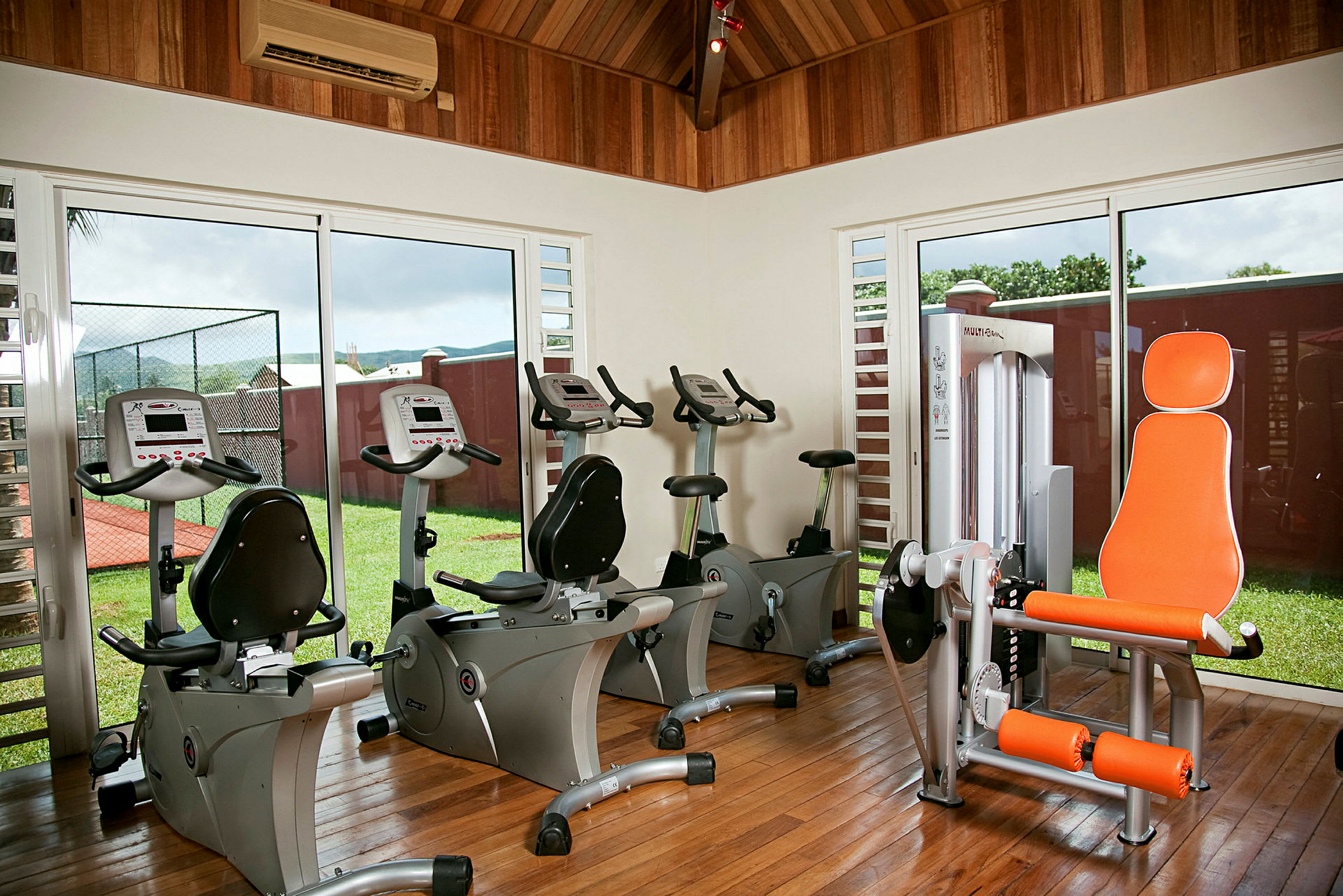 Ett gym med träningscyklar och utrustning, beläget i ett rum med träväggar och stora fönster som vetter mot grönytor. (AI-genererad text)