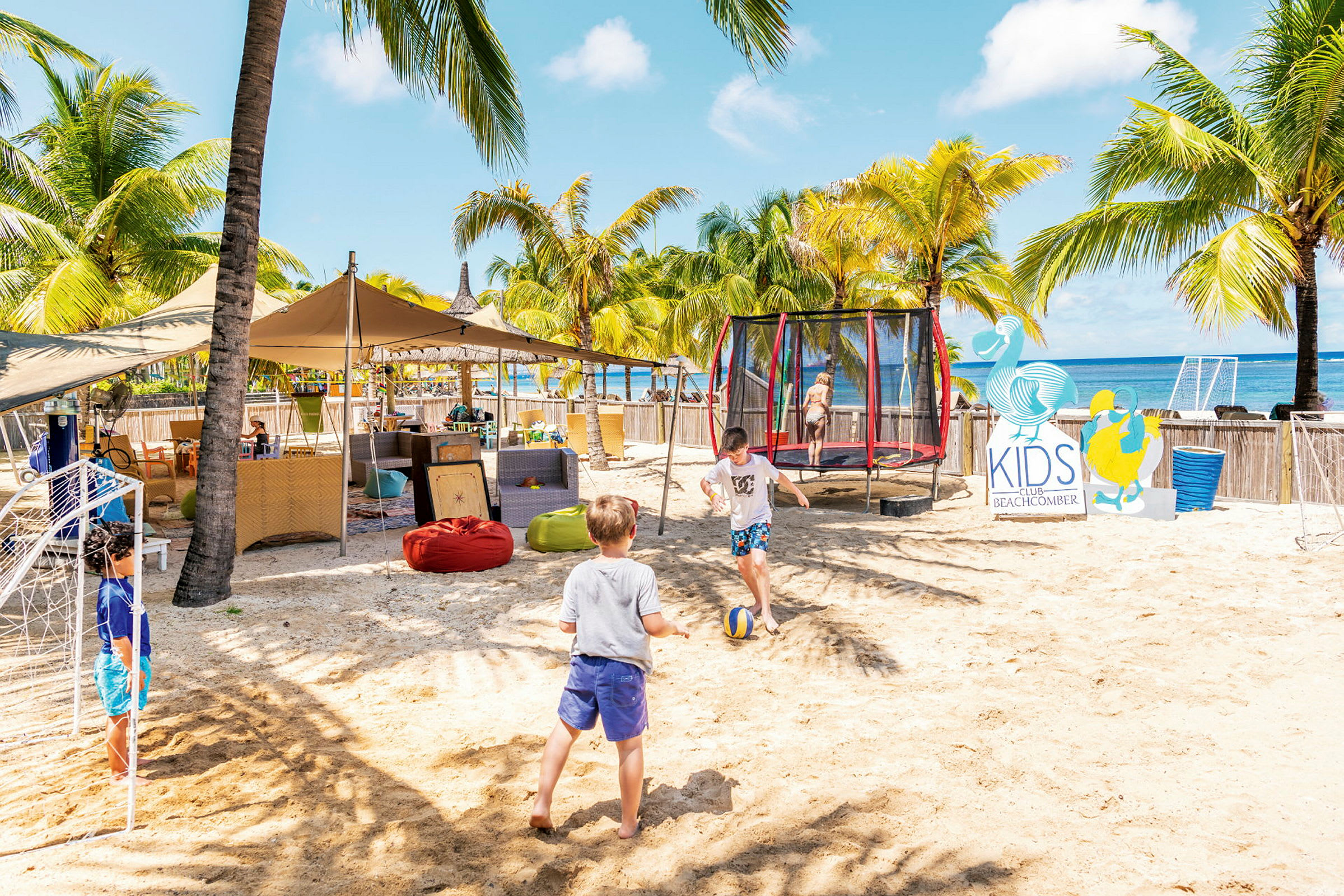 Barn leker på en sandig strand bredvid en studsmatta och skylt för Kids Club. (AI-genererad text)