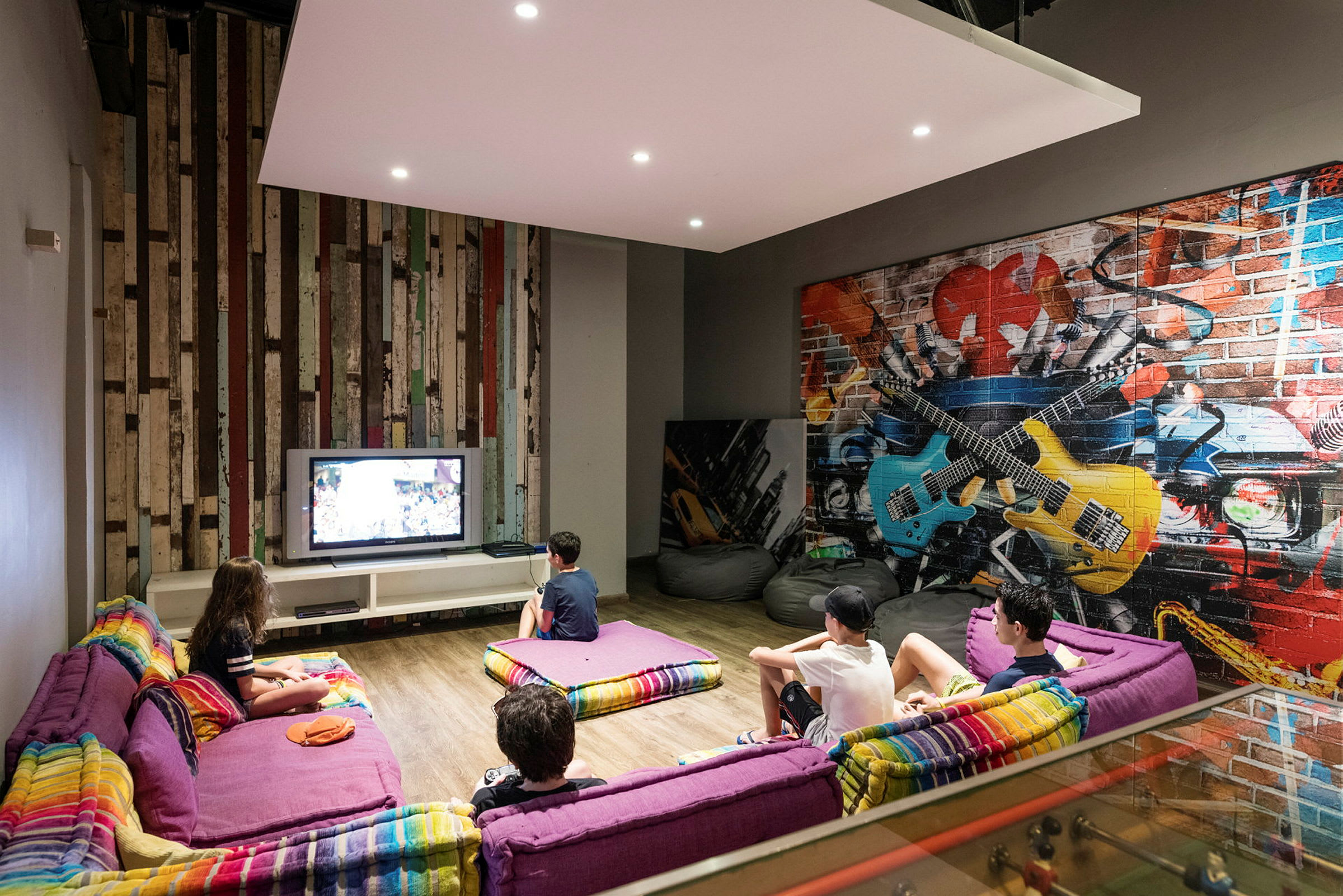 Ett rum med färgglada sittmöbler, en TV och graffiti på väggen. (AI-genererad text)