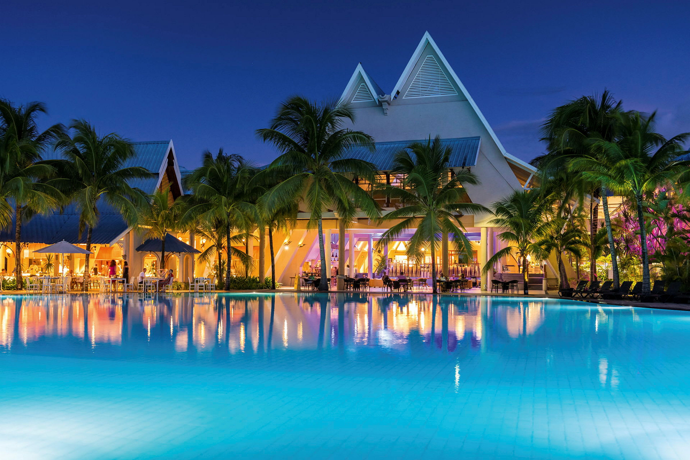 Hotellbyggnad med upplysta fönster vid en pool på kvällen. (AI-genererad text)