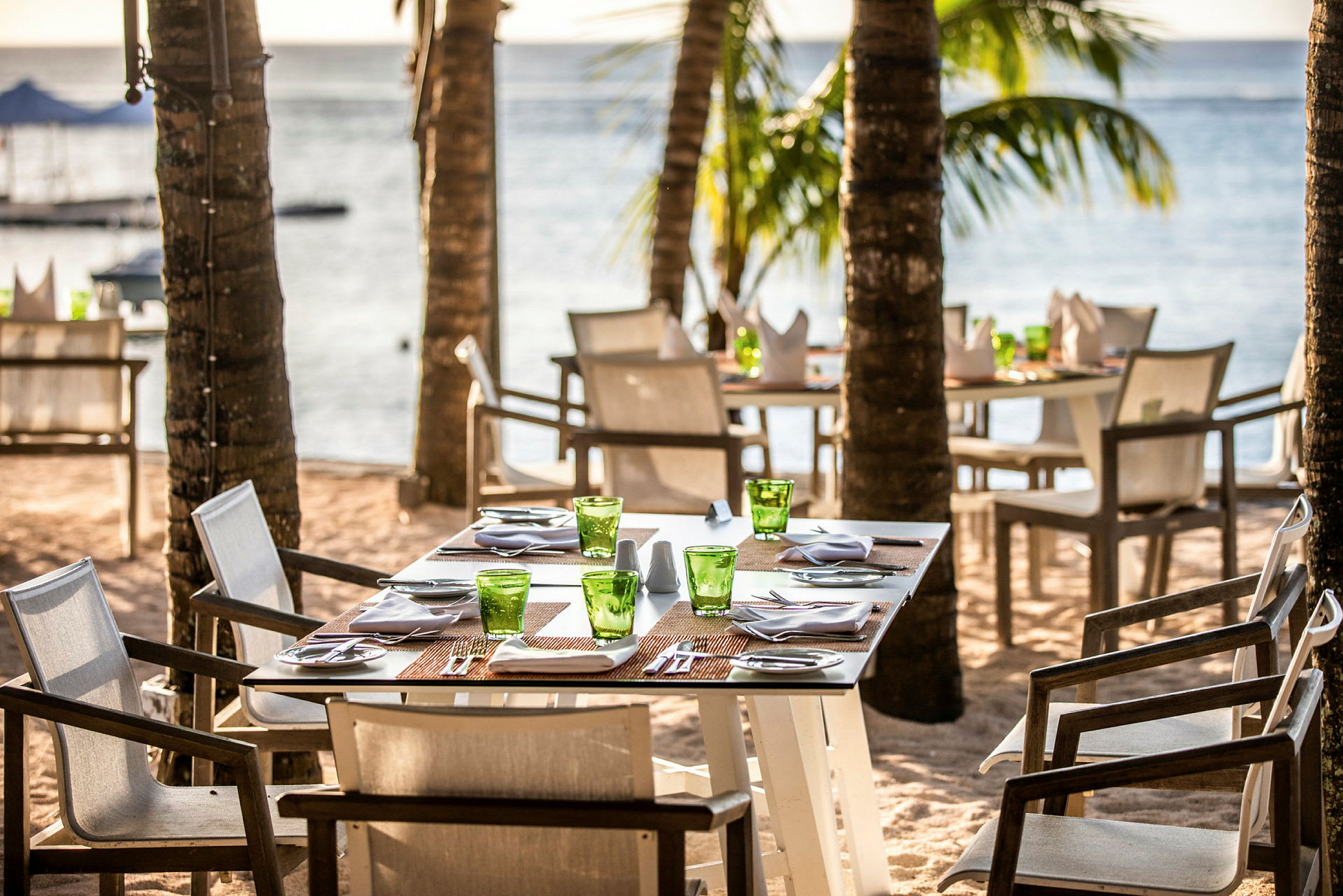 Ett strandnära café med dukade bord och grönska omkring. (AI-genererad text)