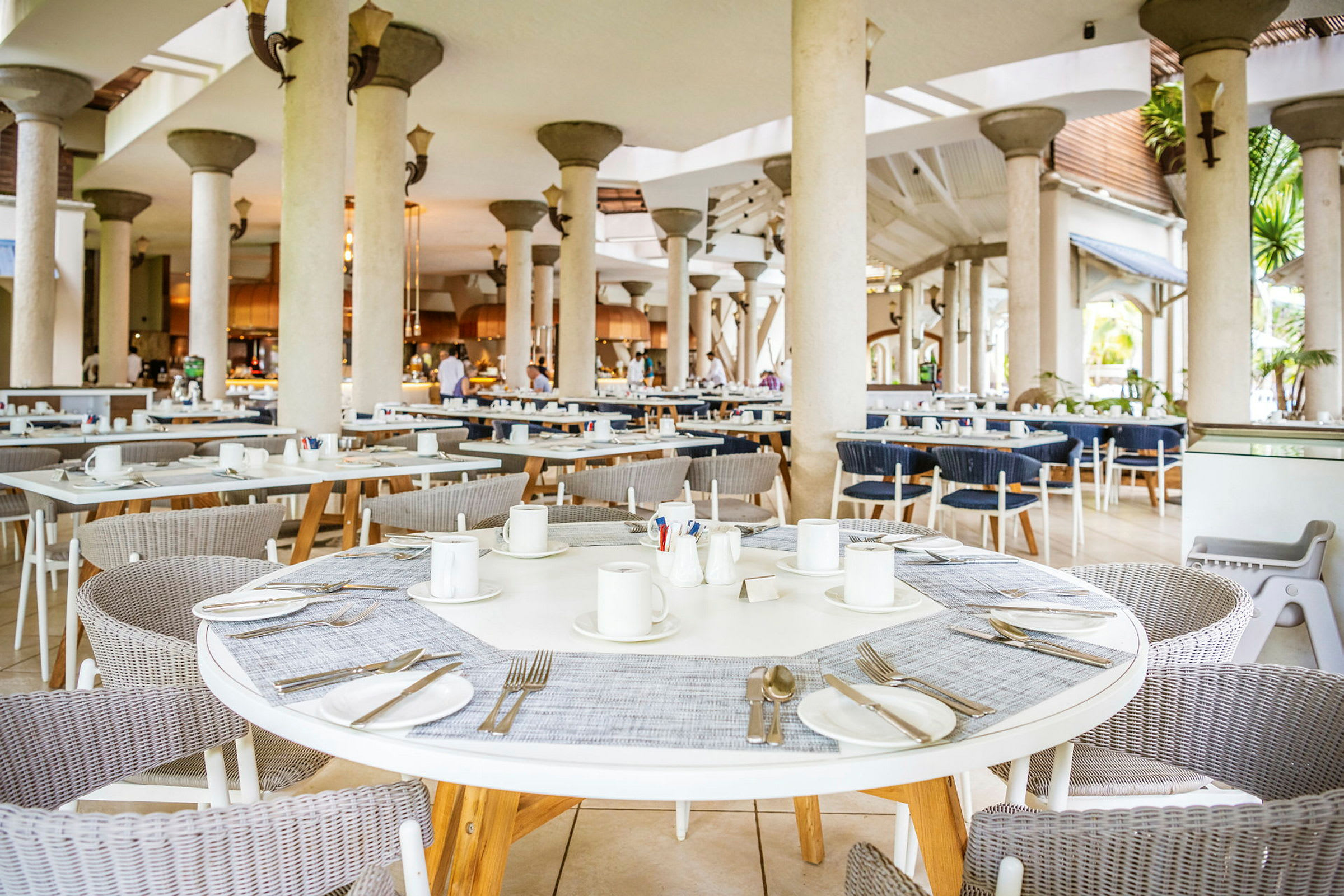 Ett luftigt restaurangområde med runda bord, stolar, och dukade platser. (AI-genererad text)