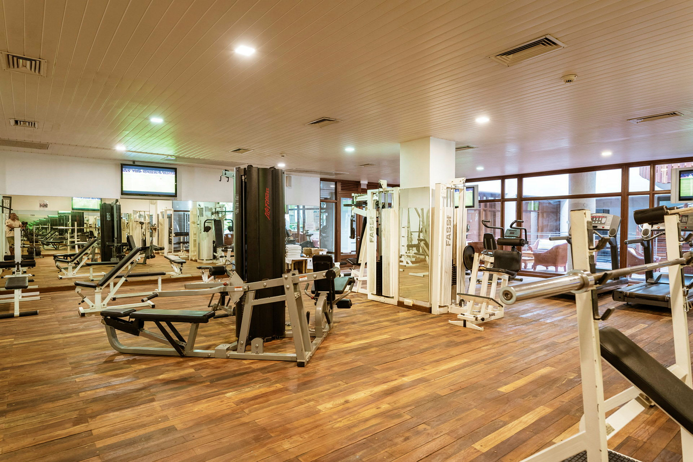 Ett gym med träningsmaskiner och vikter, beläget i ett rum med trägolv. (AI-genererad text)