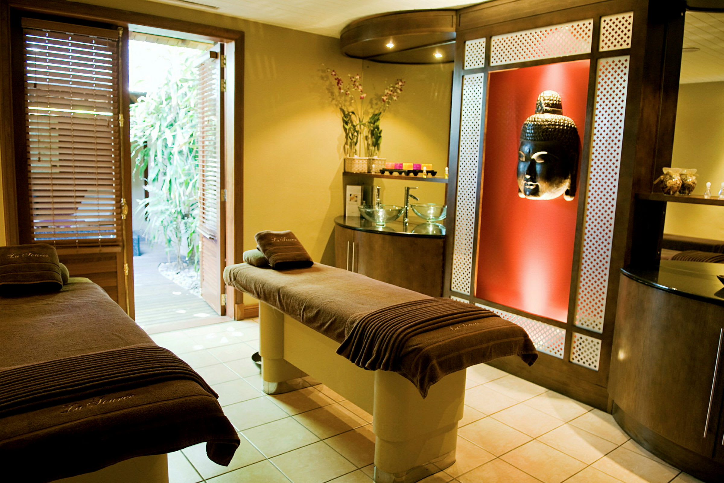 Ett spa-rum med massagebänkar, Buddha-dekoration, och öppen dörr mot trädgård. (AI-genererad text)