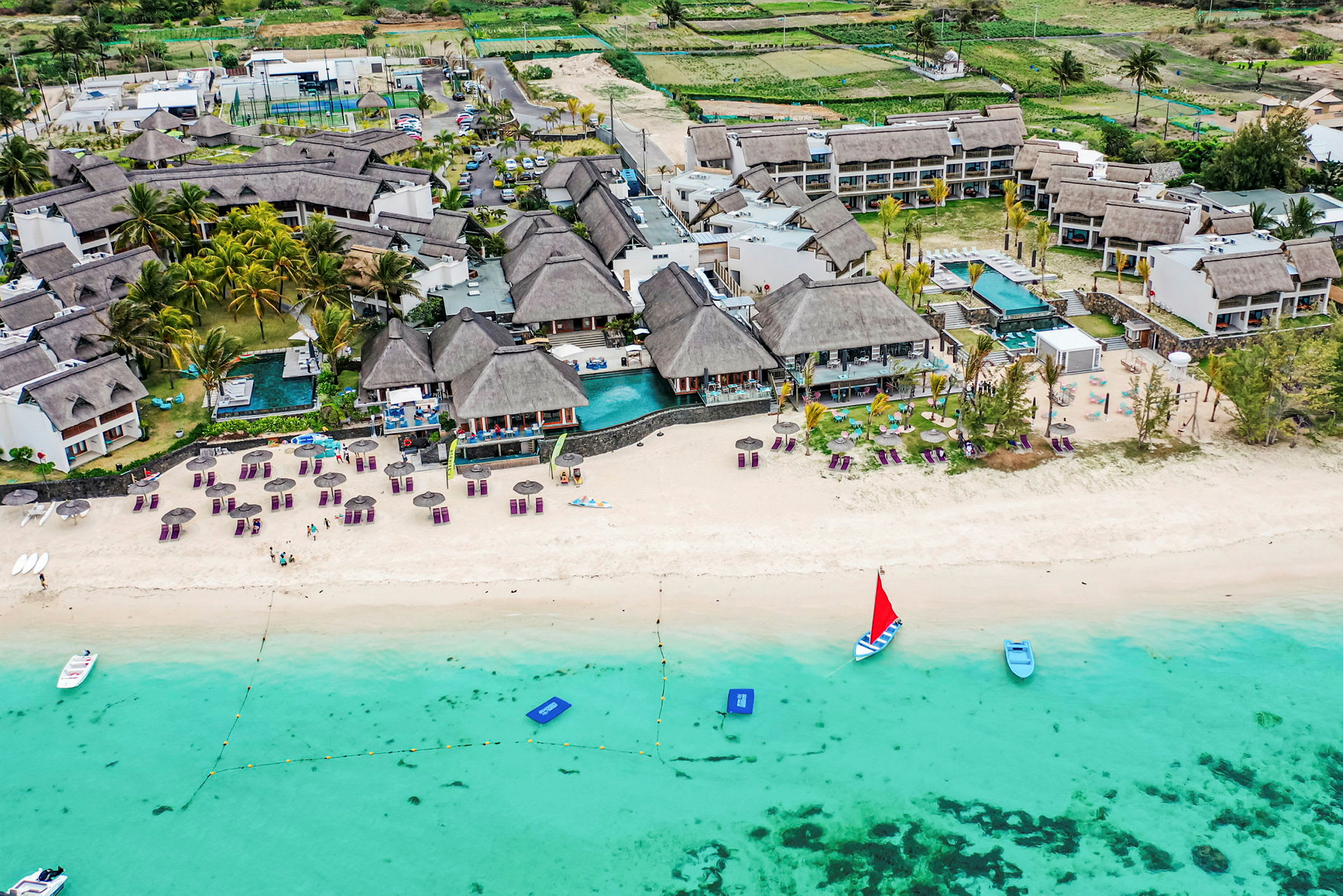 Flygfoto över en strand med solstolar, parasoller och en resort som ligger vid kanten av vattnet. (AI-genererad text)