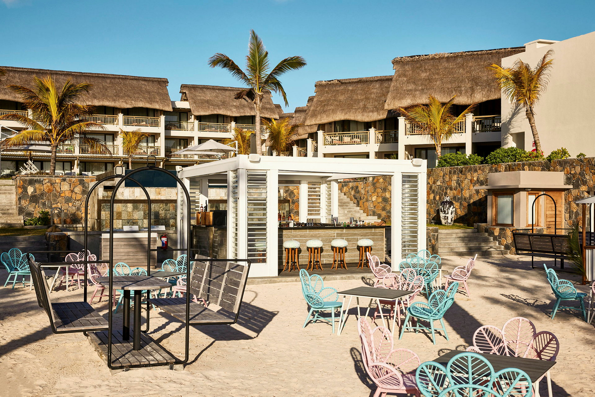 En utomhusbar med sittplatser på en sandig strand framför ett hotell. (AI-genererad text)