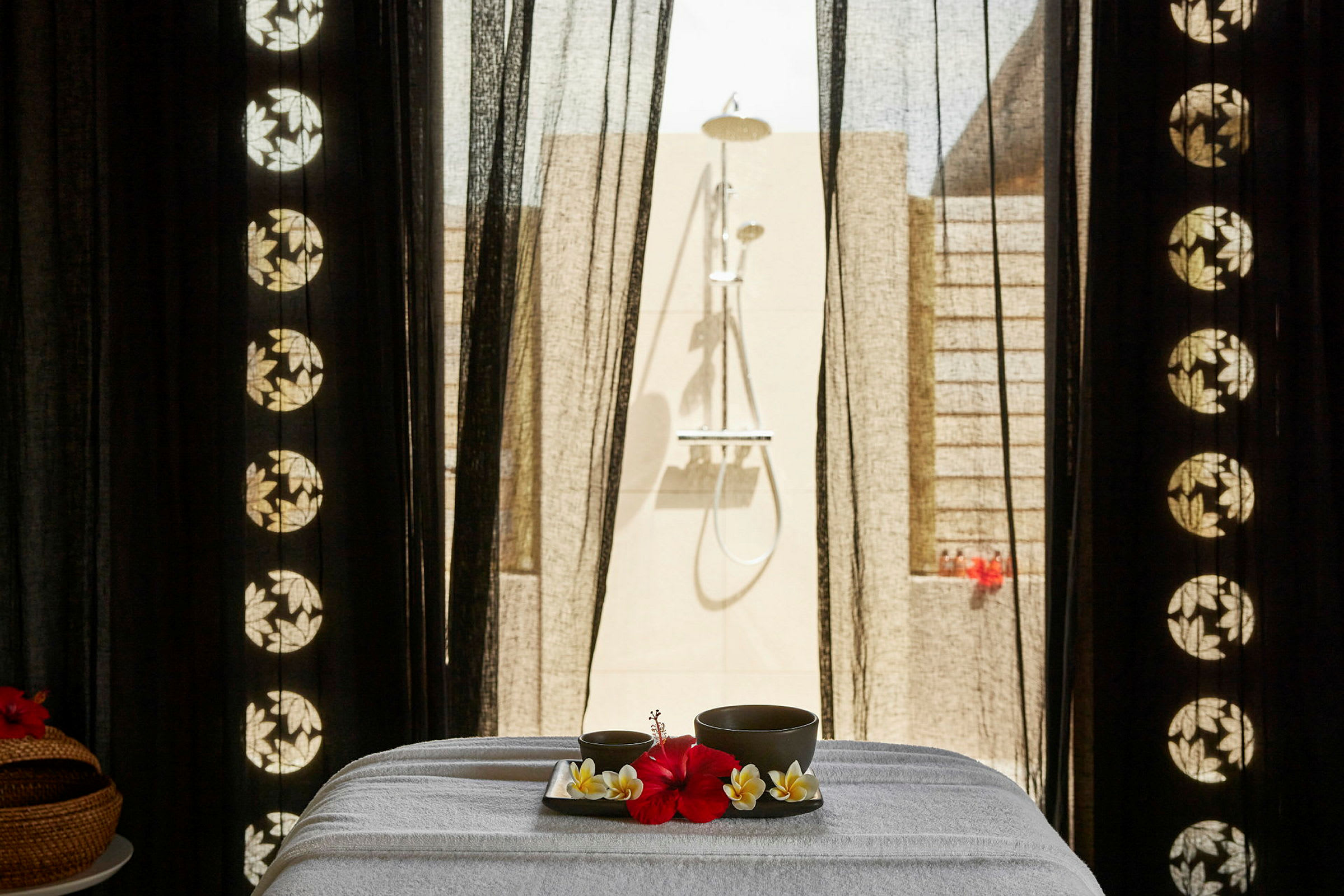 Ett spa-bord med en bricka innehållande en röd blomma och dryckeskoppar, placerad framför en utomhusdusch. (AI-genererad text)