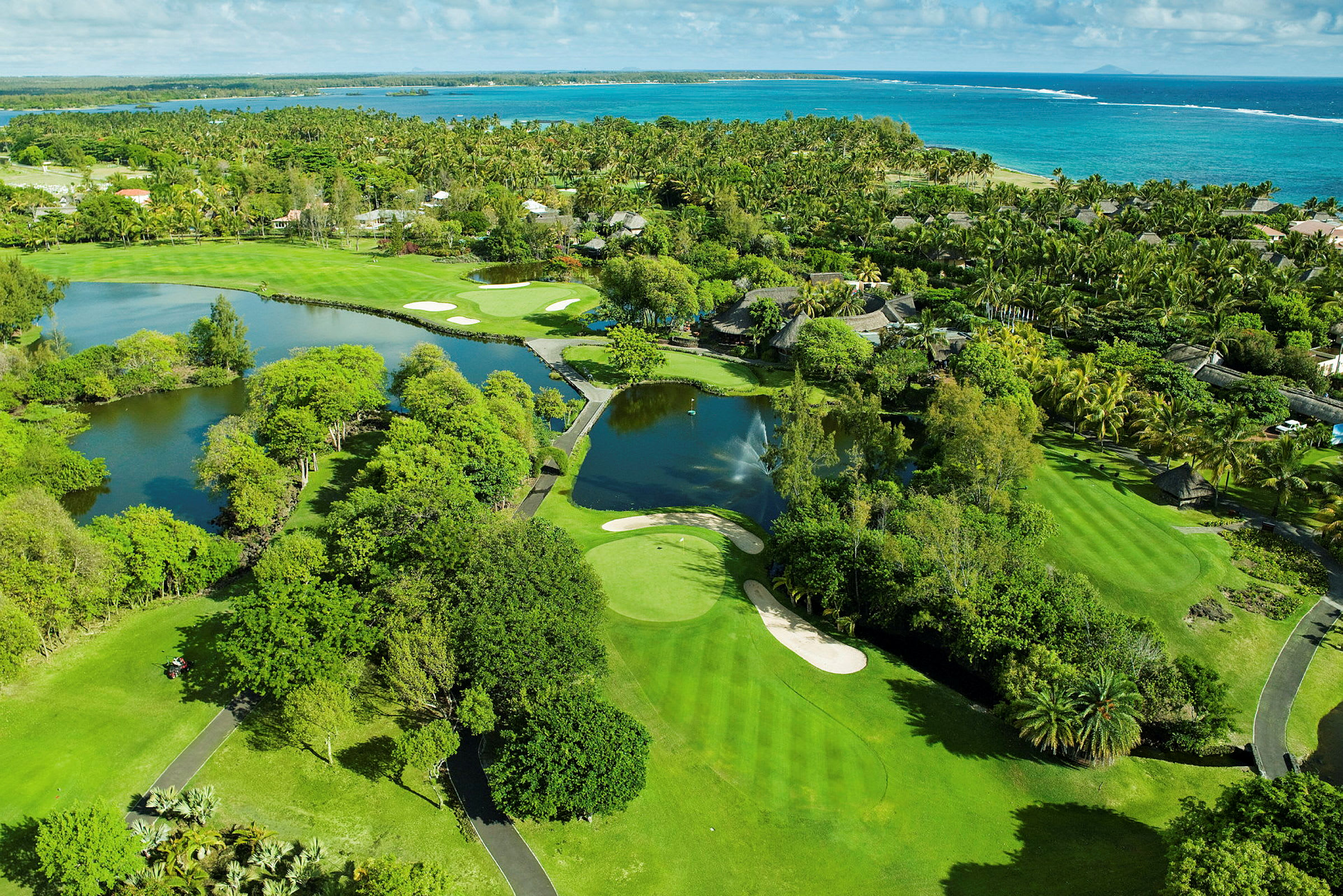 Flygfoto över en grön golfbana vid havet med omgivande träd och vattenytor. (AI-genererad text)