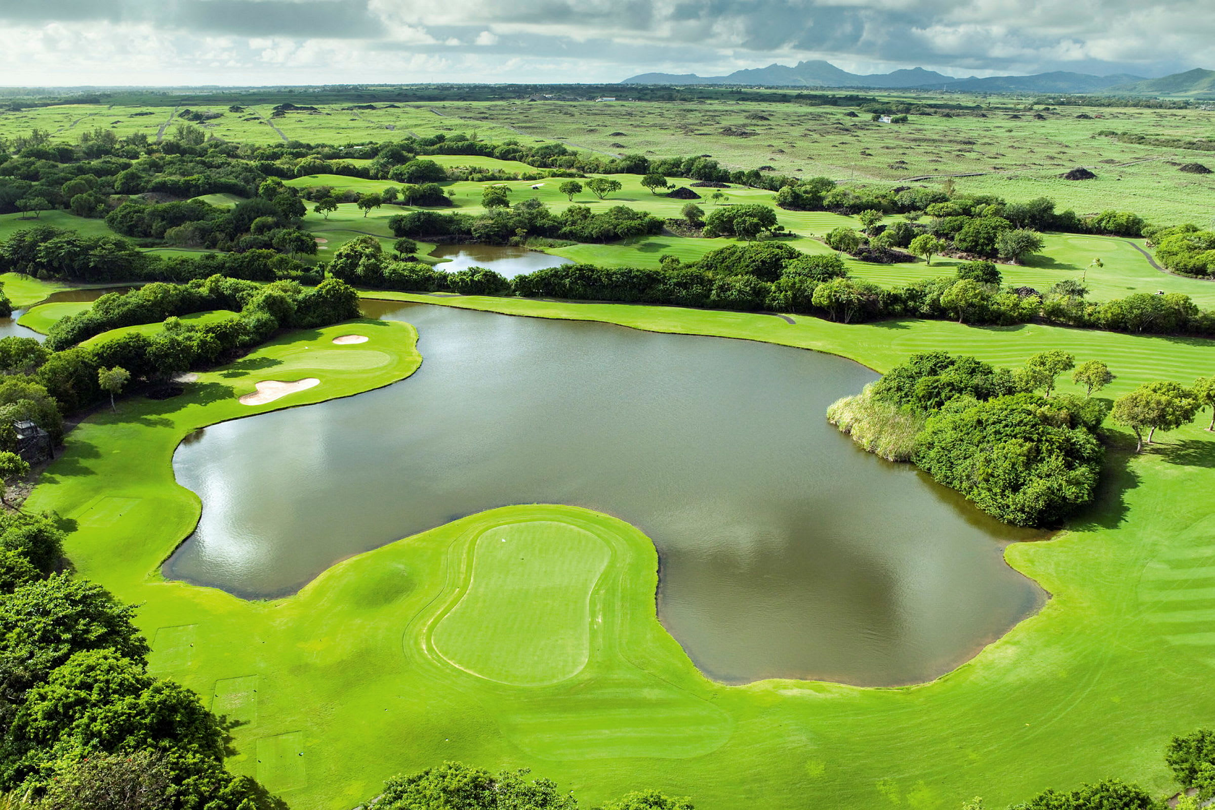 En vy över en grön golfbana med vattenhinder och omgivande landskap. (AI-genererad text)