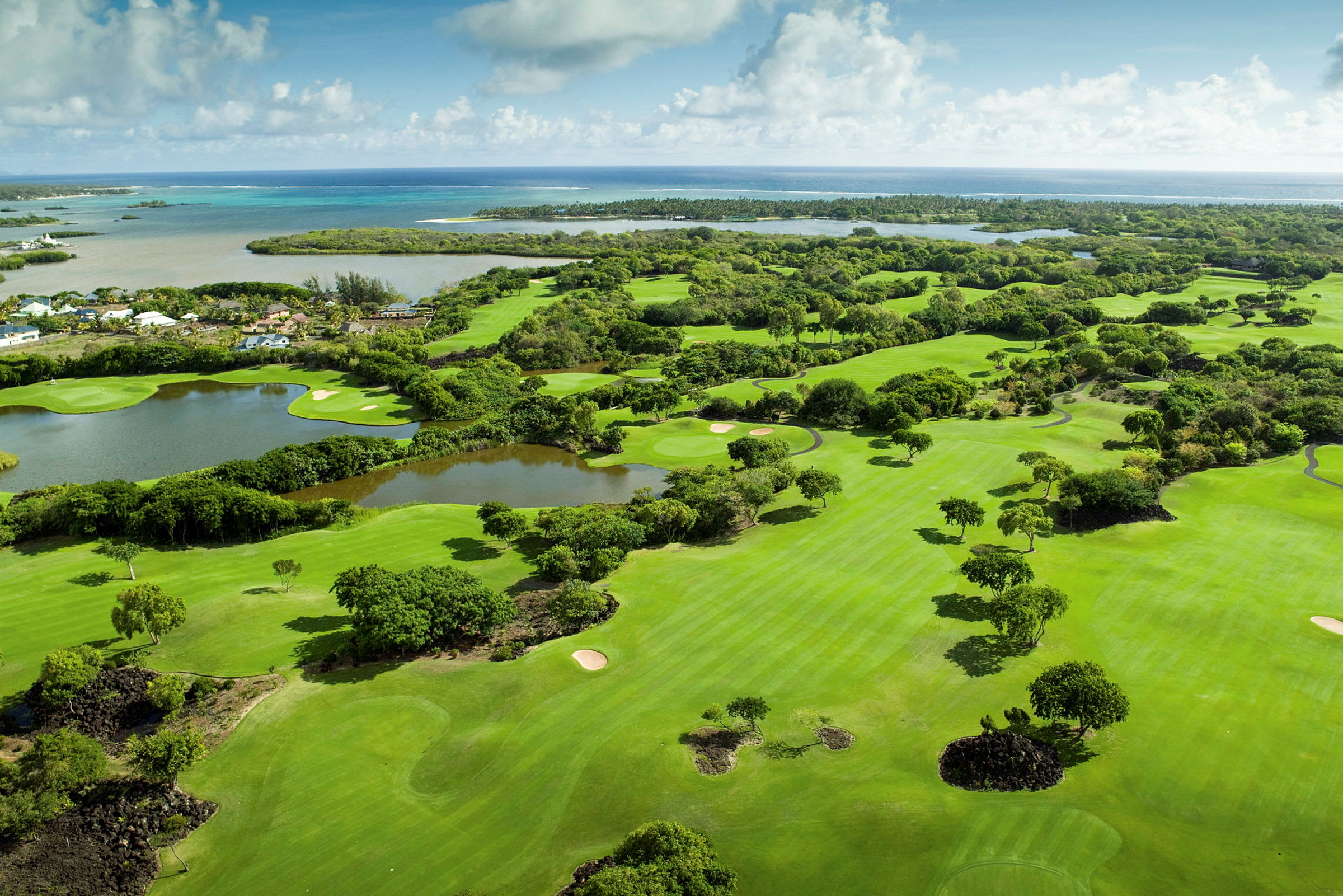 Flygfoto över en golfbana omgiven av grönska med havet i bakgrunden. (AI-genererad text)