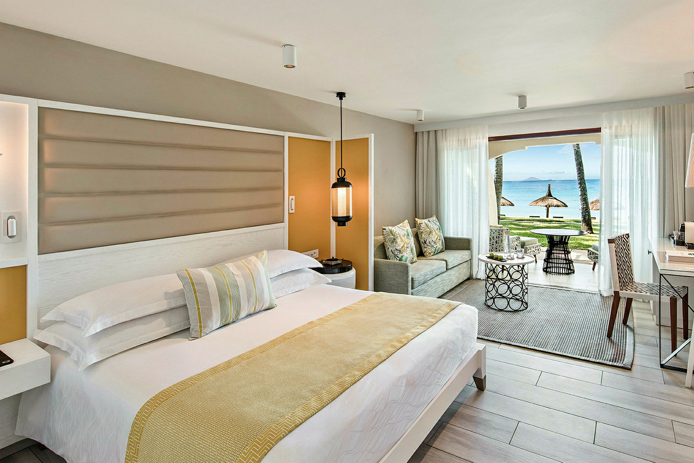 Hotellrum med ett bäddat säng, sittmöbler och en utsikt mot stranden med parasoller. (AI-genererad text)