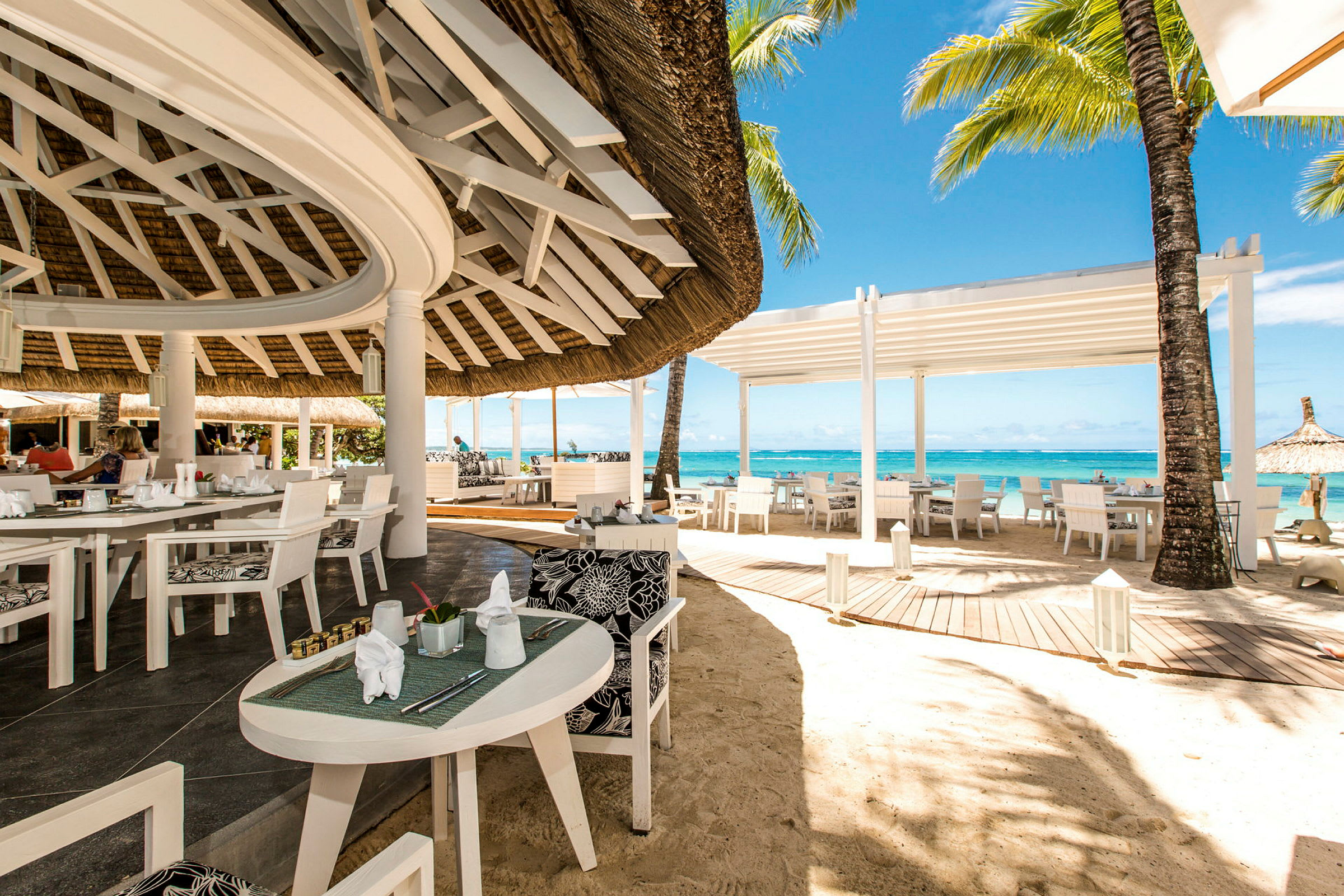 En öppen restaurang vid stranden med vita möbler och utsikt över havet. (AI-genererad text)