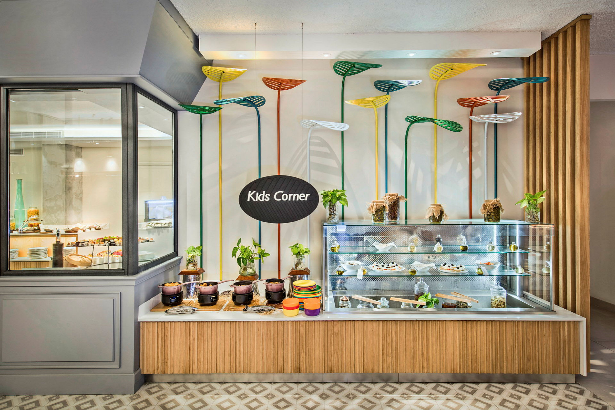 Ett matområde för barn märkt med skylten "Kids Corner" med en visningsdisk fylld med måltider och dekorerad med färgglada växtliknande designelement. (AI-genererad text)