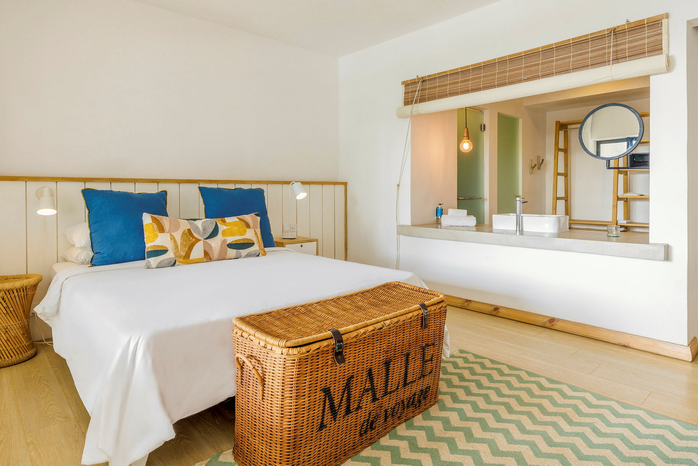 Ett ljust hotellrum med en dubbelsäng och en korg vid fotändan. (AI-genererad text)