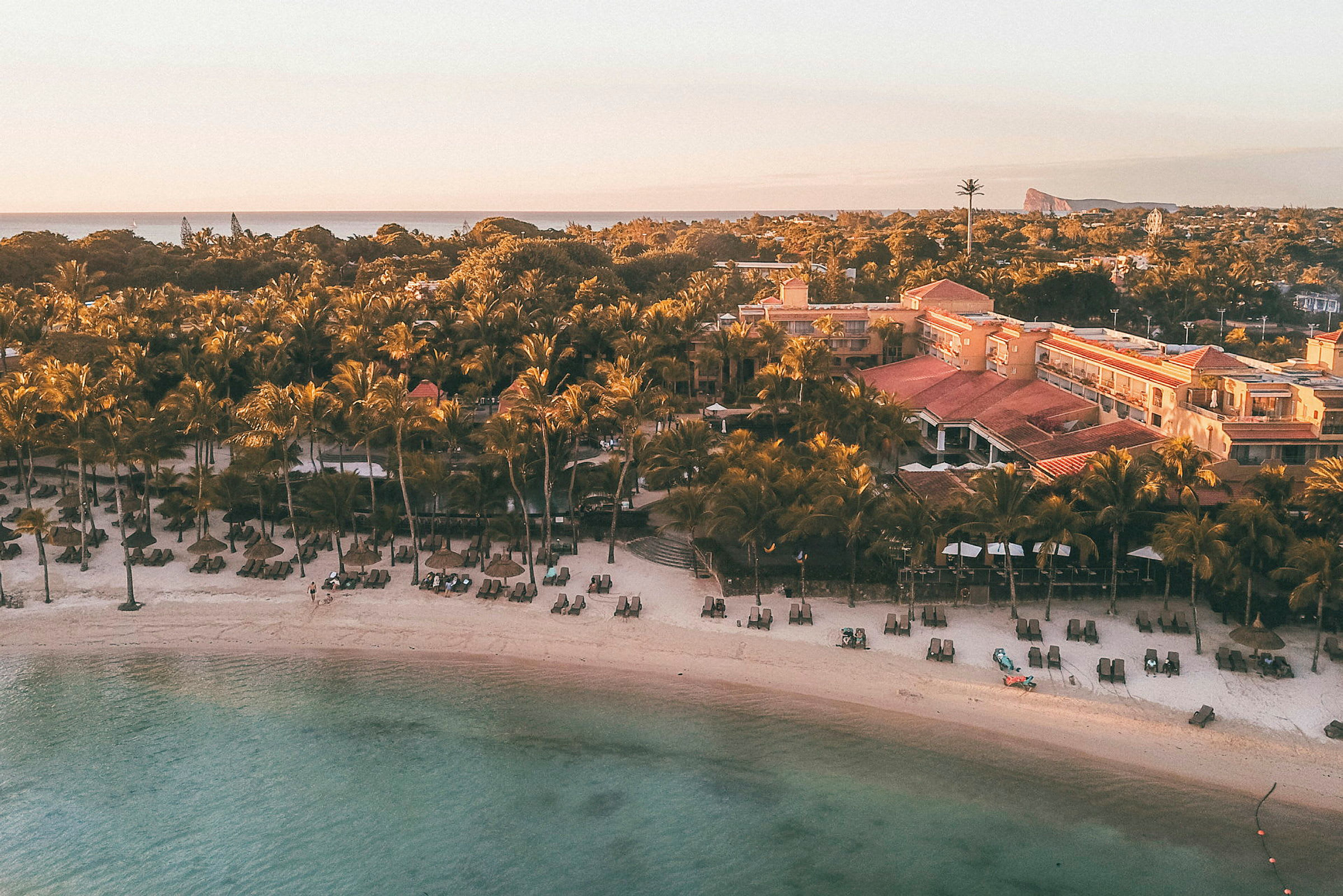 Strand med solstolar och parasoll framför en resort och palmer vid havet. (AI-genererad text)