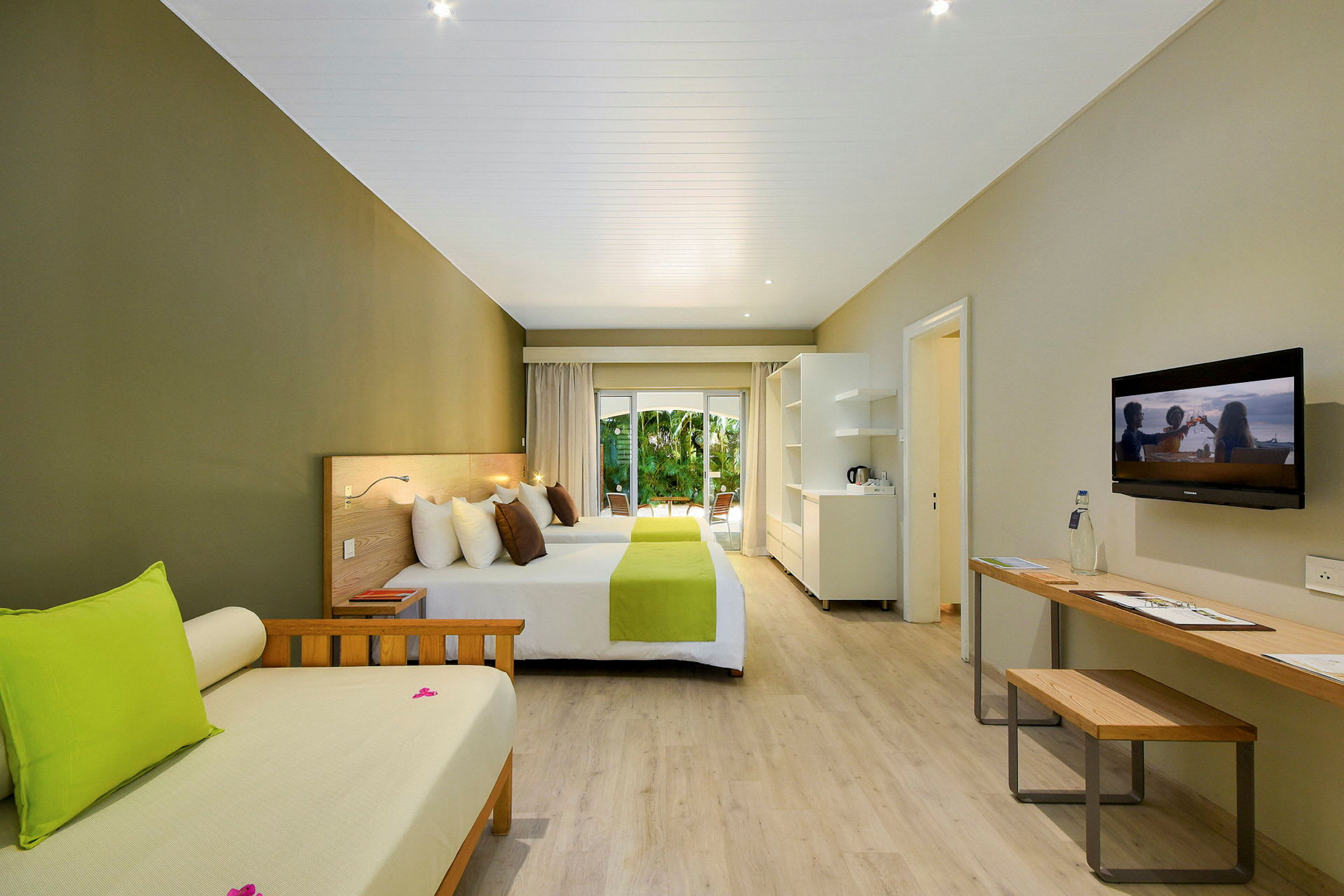 Hotellrum med två sängar, en soffa, ett skrivbord och en balkong med trädgårdsutsikt. (AI-genererad text)