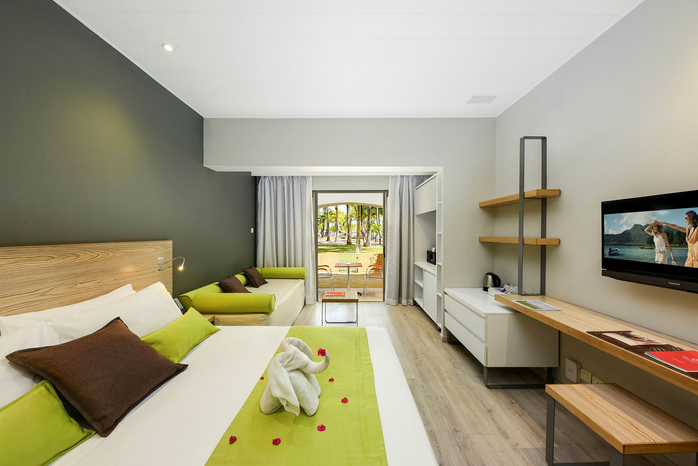 Modernt hotellrum med säng, skrivbord, soffa och utsikt mot en trädgård. (AI-genererad text)