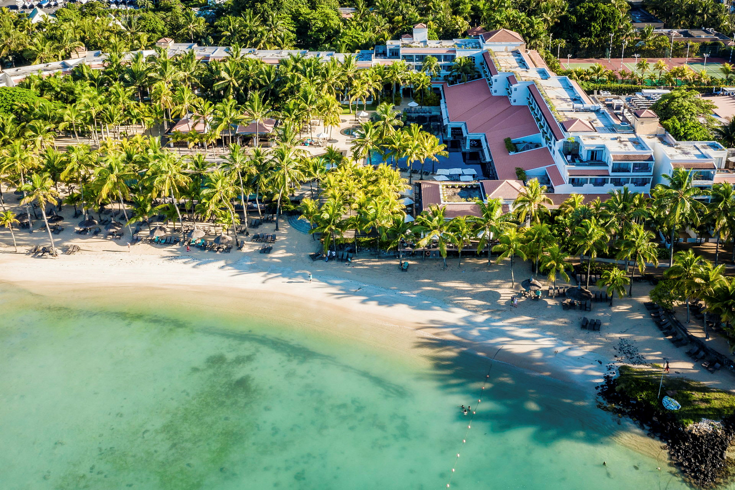 Flygbild av en sandstrand vid ett hotell omgiven av palmer. (AI-genererad text)
