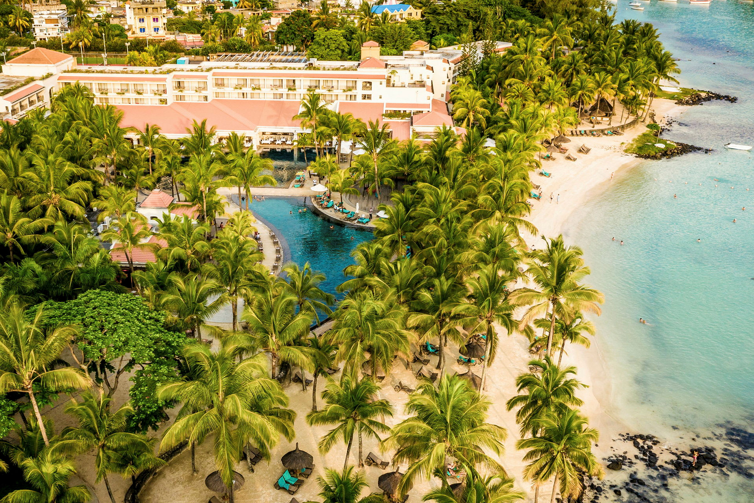 Utsikt över ett semesterhotell med en pool, palmträd och strand vid havet. (AI-genererad text)