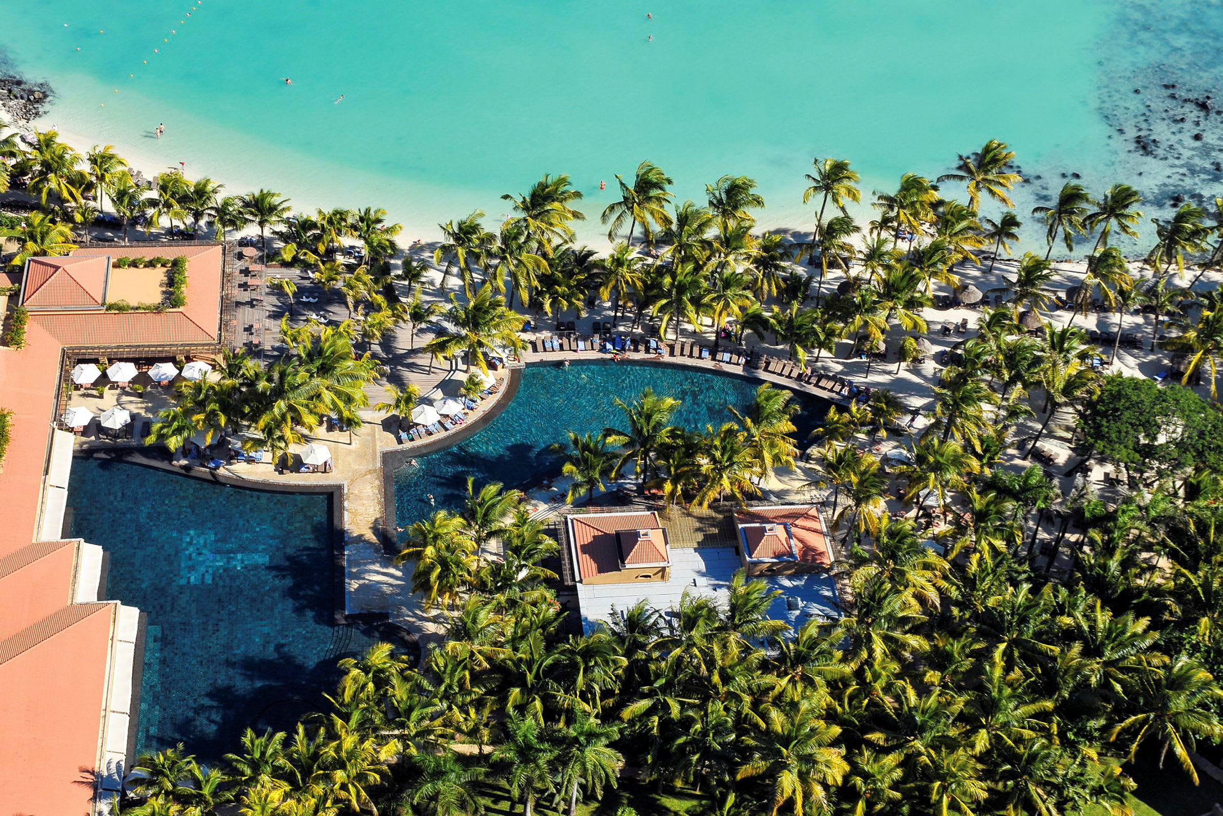 Flygfoto av en tropisk resort med pool, palmer och stranden vid det turkosa havet. (AI-genererad text)