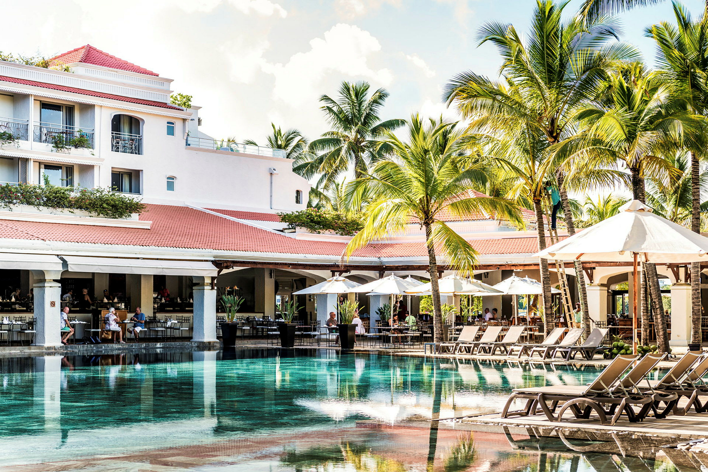 En pool omgiven av solstolar och parasoller på ett hotell med palmer i bakgrunden. (AI-genererad text)