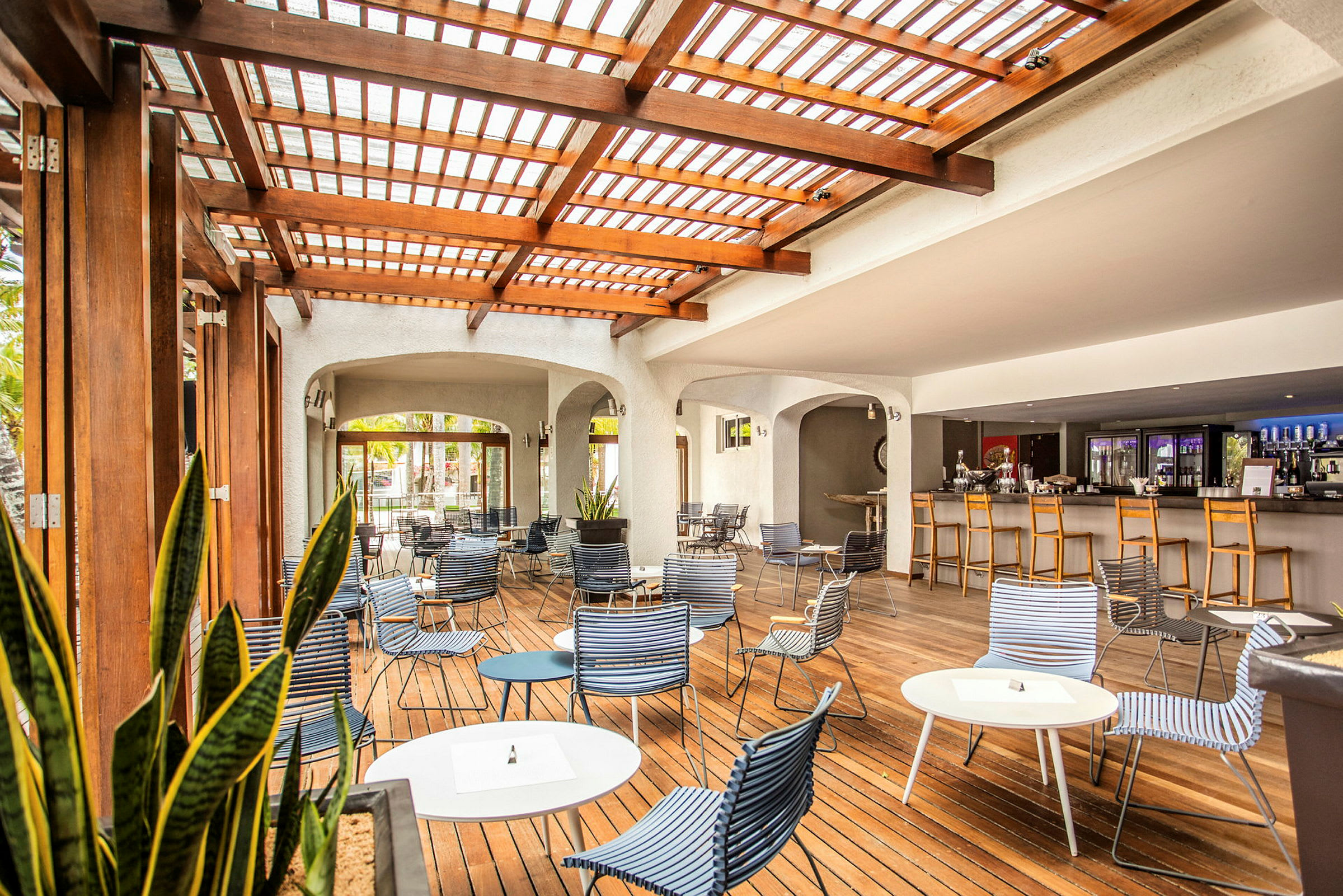 En utomhuslounge med träpergola, sittplatser och bord, samt en bar i bakgrunden. (AI-genererad text)