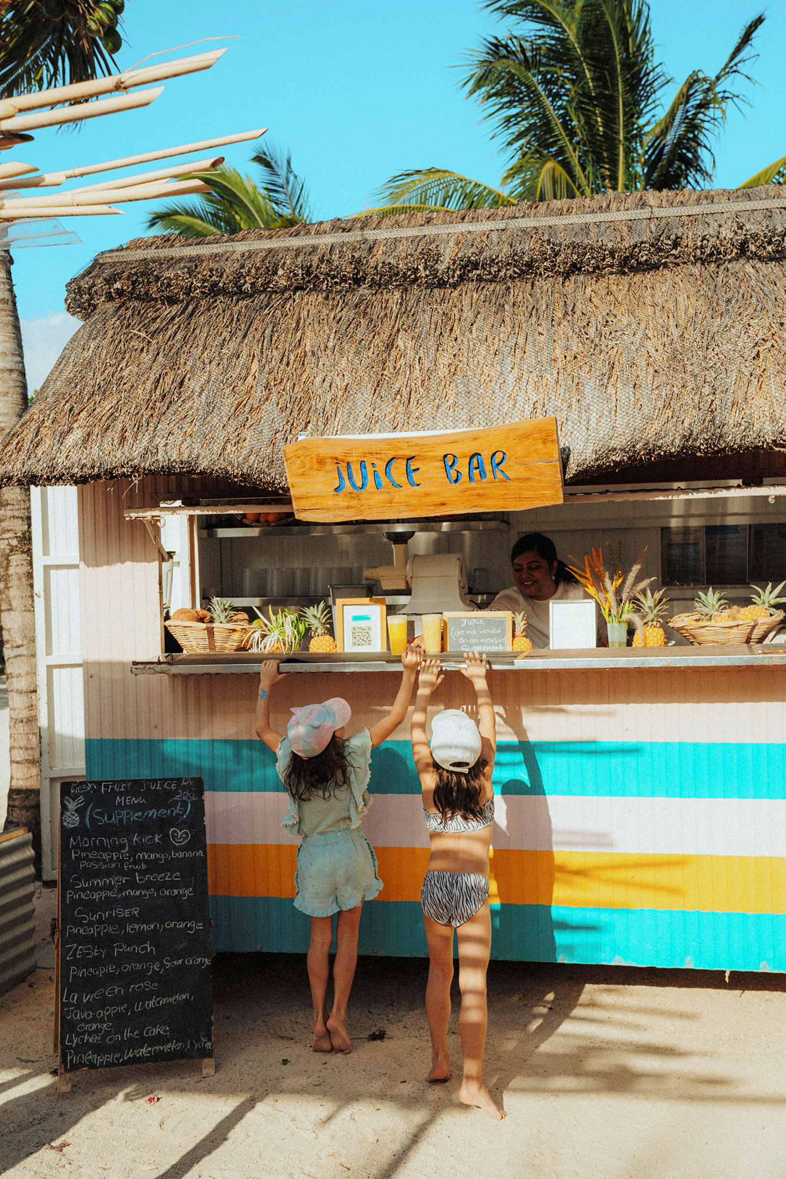 Två personer står vid en juicebar med halmtak på en solig plats. (AI-genererad text)