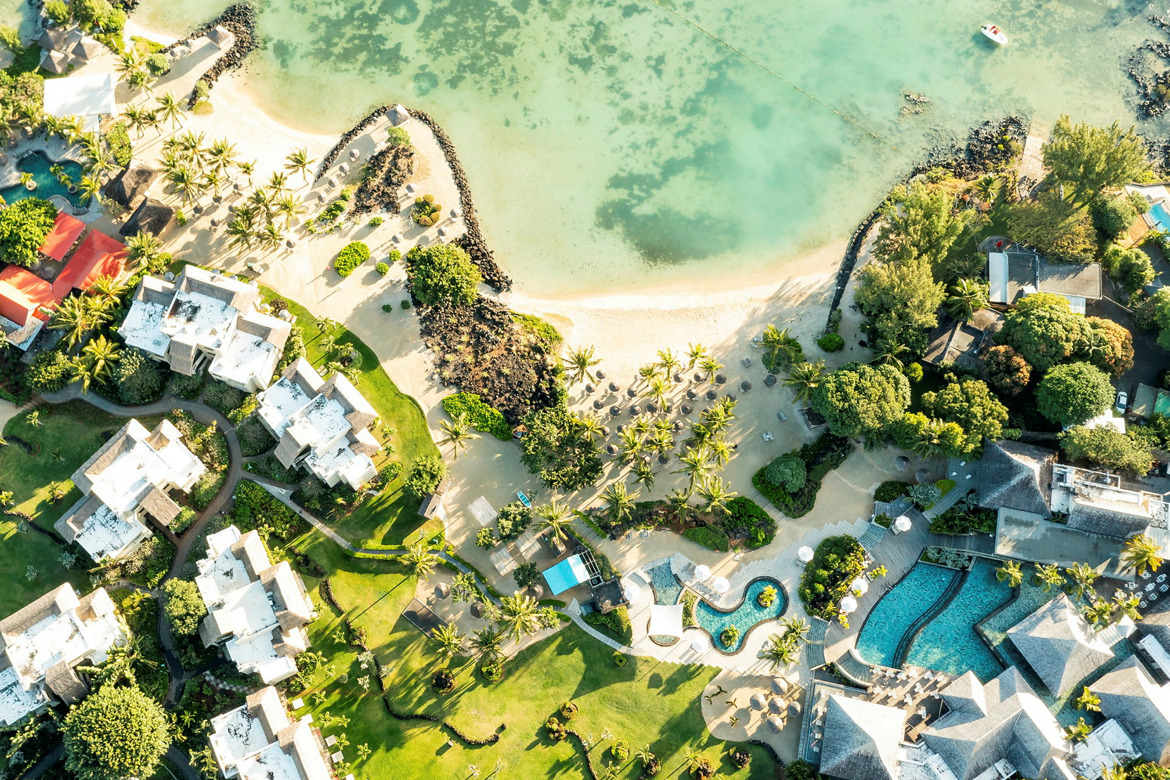 Flygfoto av hotellbyggnader och poolområden längs en sandstrand med palmer. (AI-genererad text)