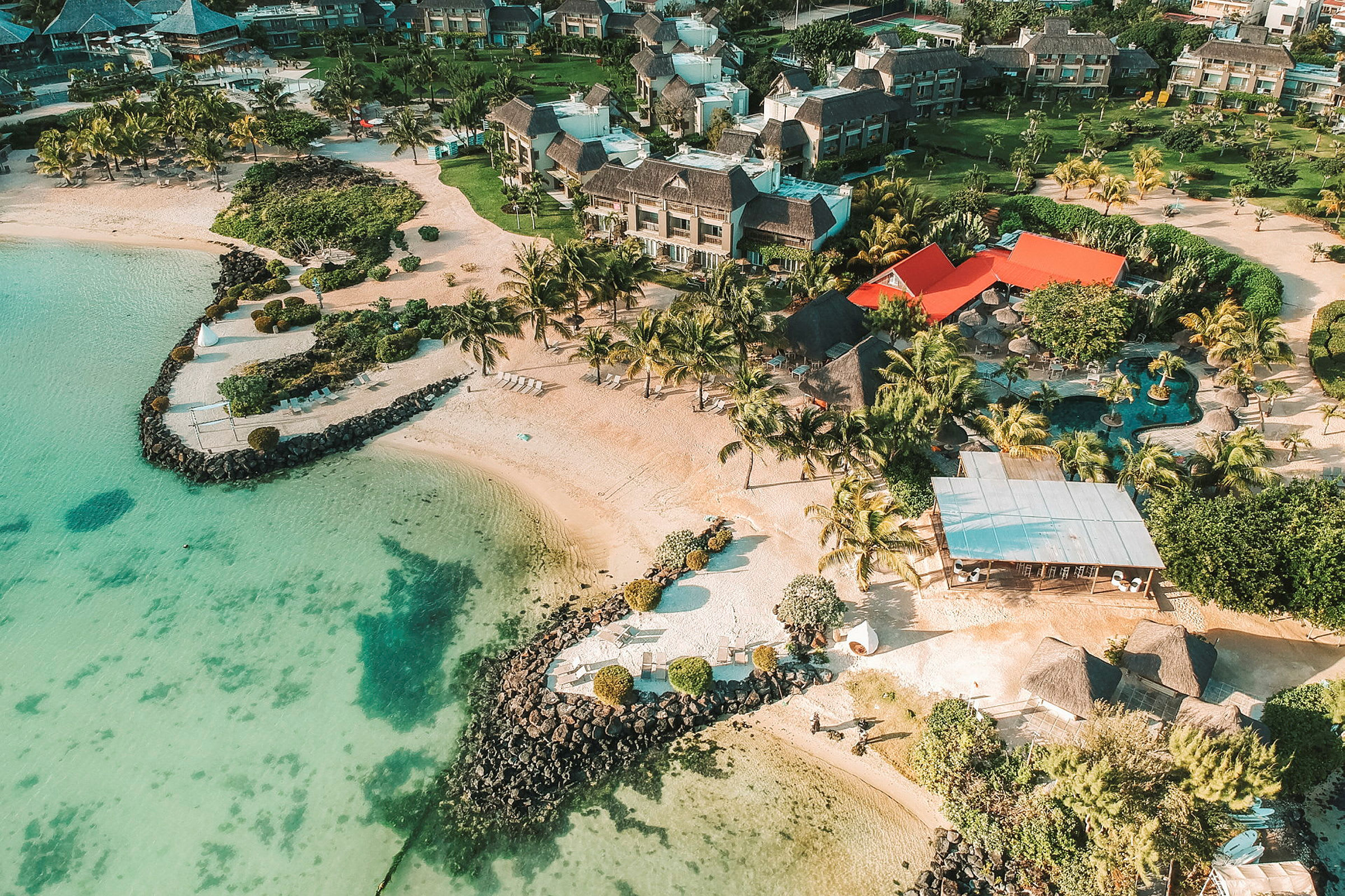 Flygfoto av en semesterort vid en sandstrand med palmer och byggnader. (AI-genererad text)