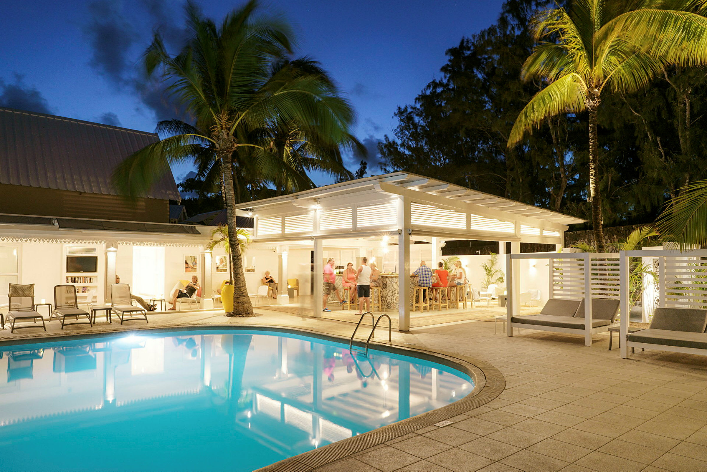 En upplyst hotellpool med solstolar och palmer vid dusk. (AI-genererad text)