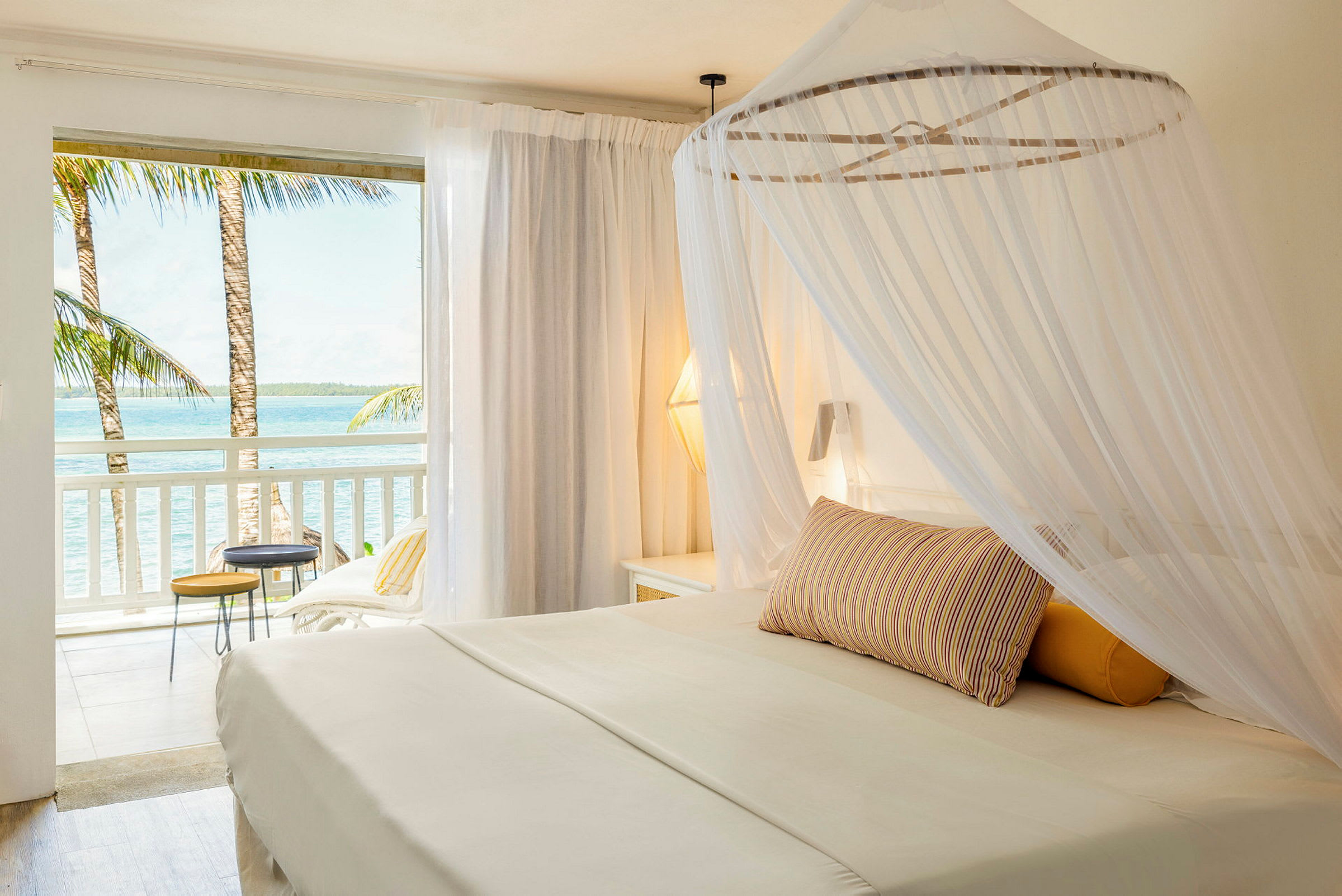 En ljus hotellsvit med en himmelssäng och utsikt över havet från balkongen. (AI-genererad text)