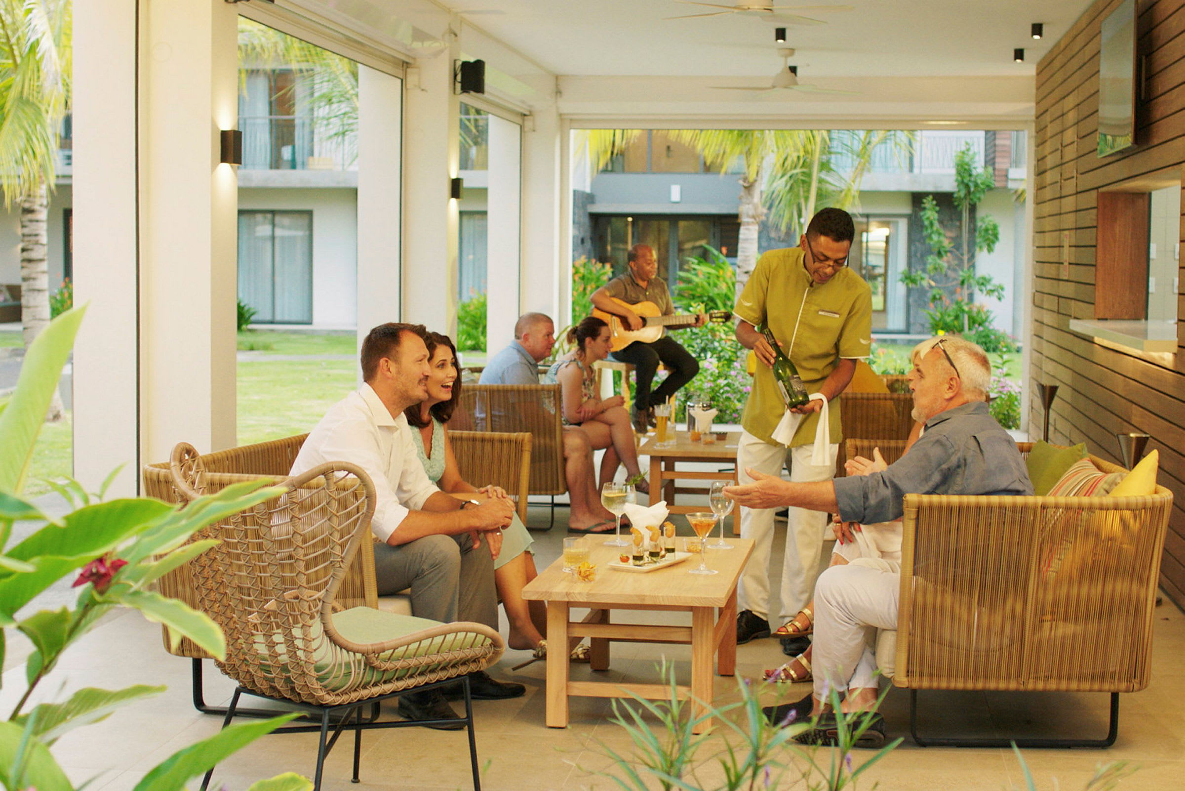 En hotellterrass med sittgrupper, där serveras drycker och någon spelar gitarr. (AI-genererad text)