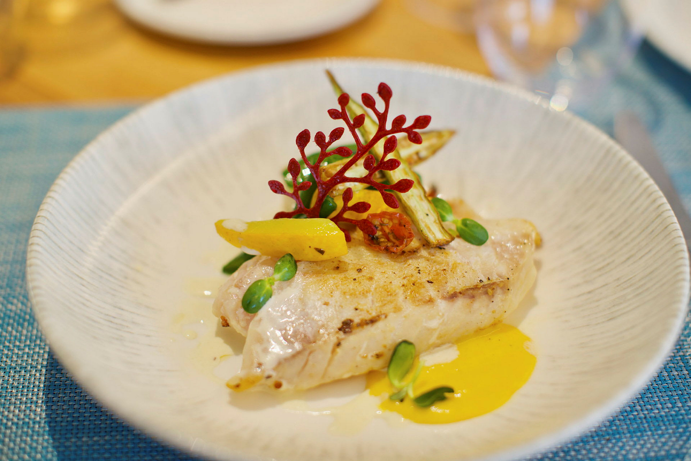 En tallrik med en elegant upplagd rätt bestående av grillad fiskfilé med grönsaker och sås. (AI-genererad text)