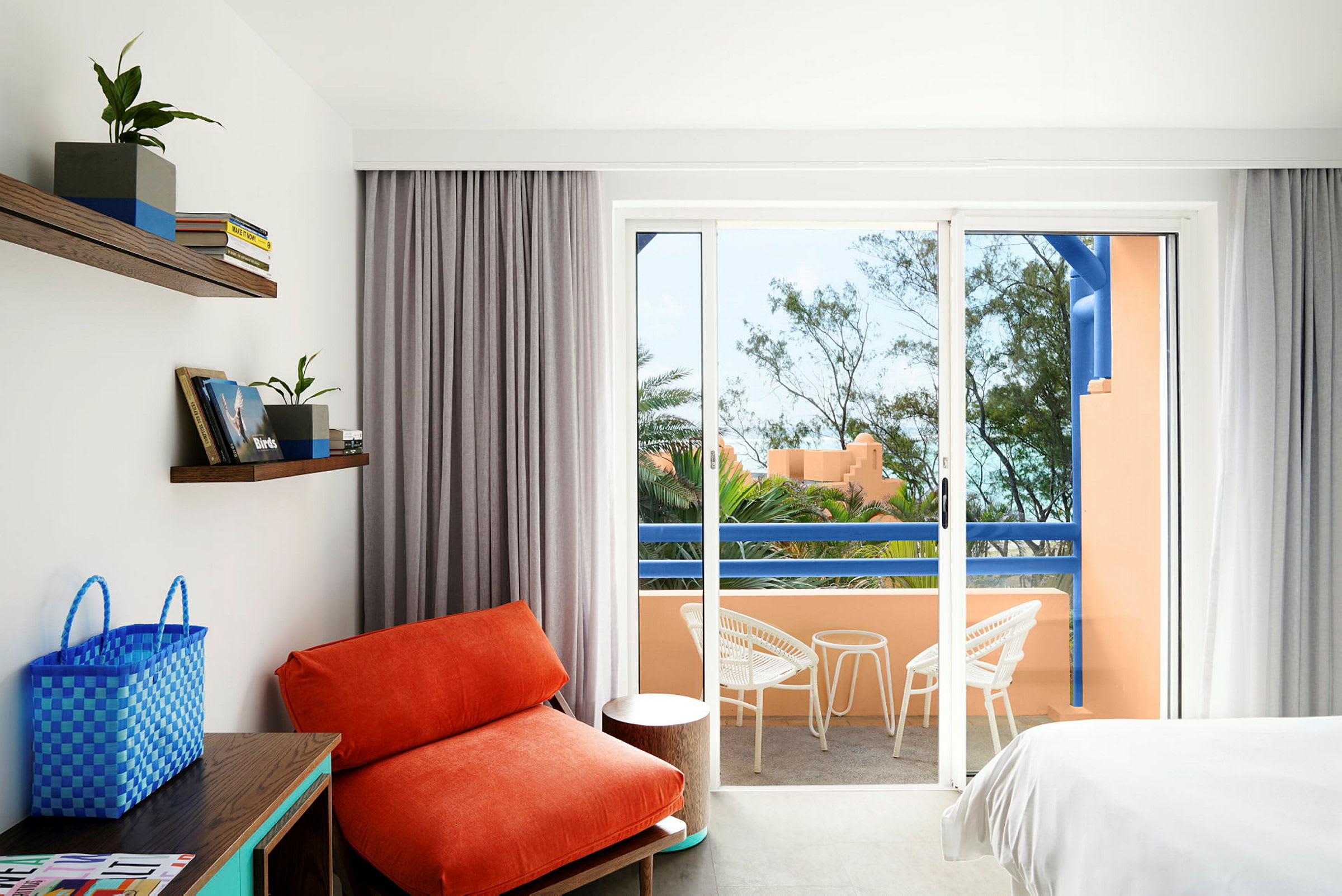 Ett hotellrum med en orange fåtölj, vita möbler på en balkong och utsikt över grönska. (AI-genererad text)