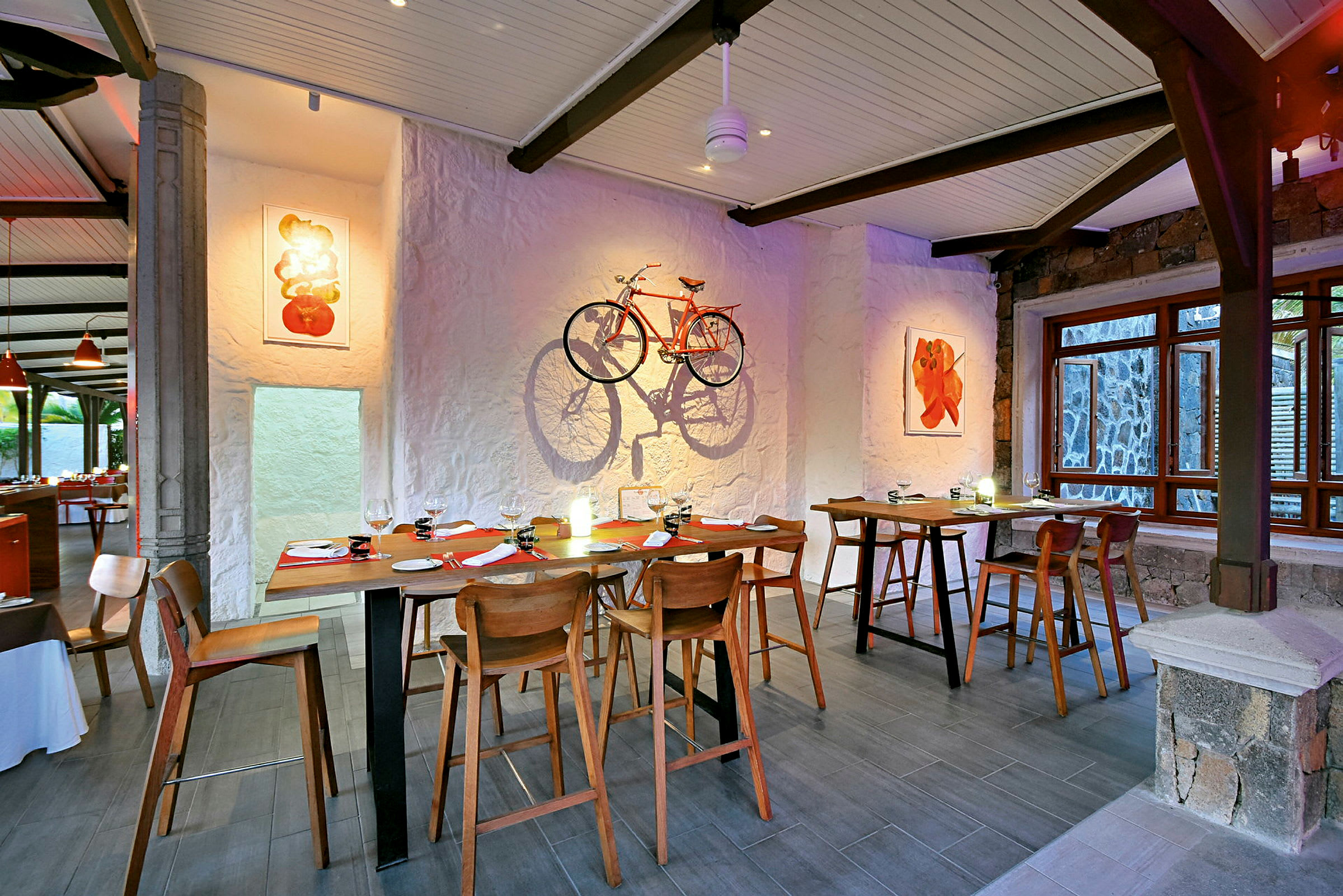 Inredning av restaurang med träbord och stolar, konst på väggarna och en orange cykel dekorerad som väggkonst. (AI-genererad text)