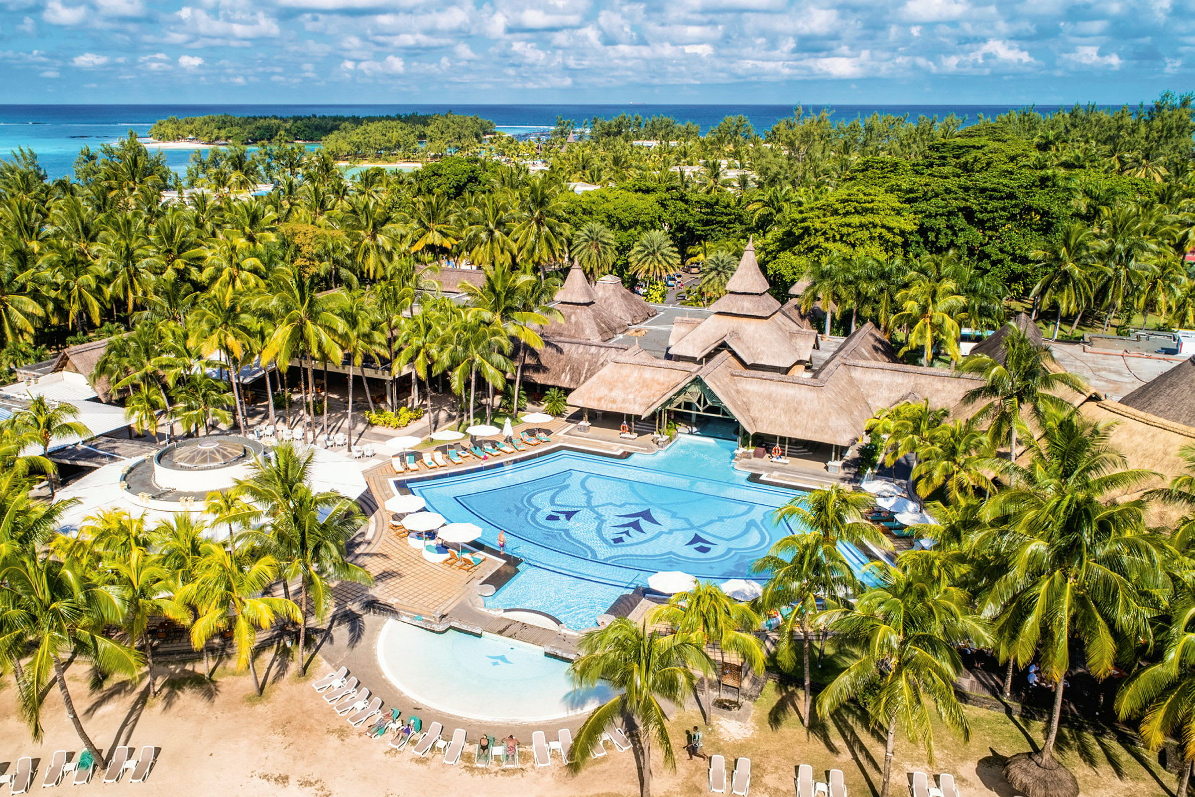 En tropisk resort med en stor pool omgiven av palmer och byggnader med traditionella tak. (AI-genererad text)