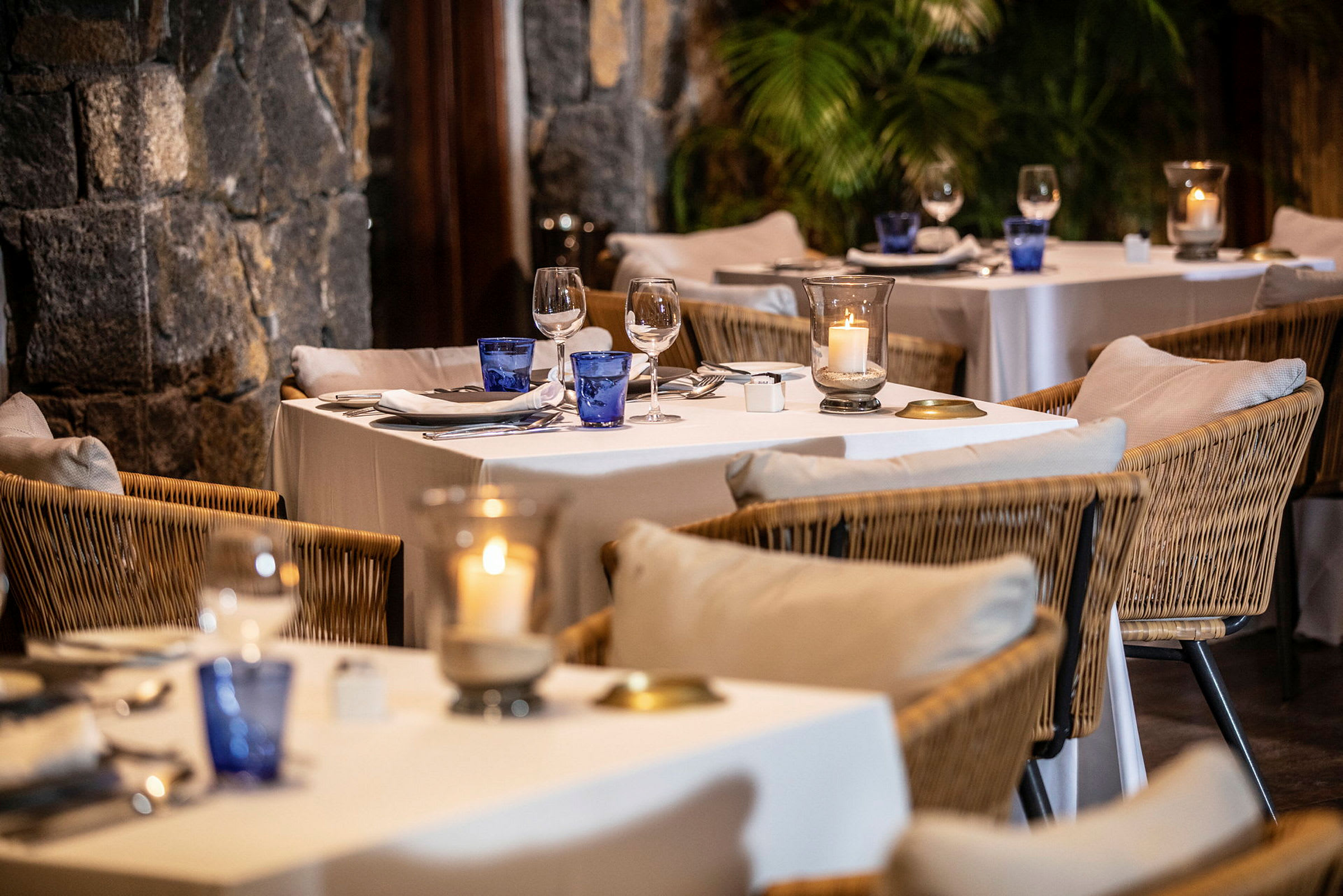 Ett elegant dukat bord i en restaurang med stolar av rotting och vita linnedukar. (AI-genererad text)