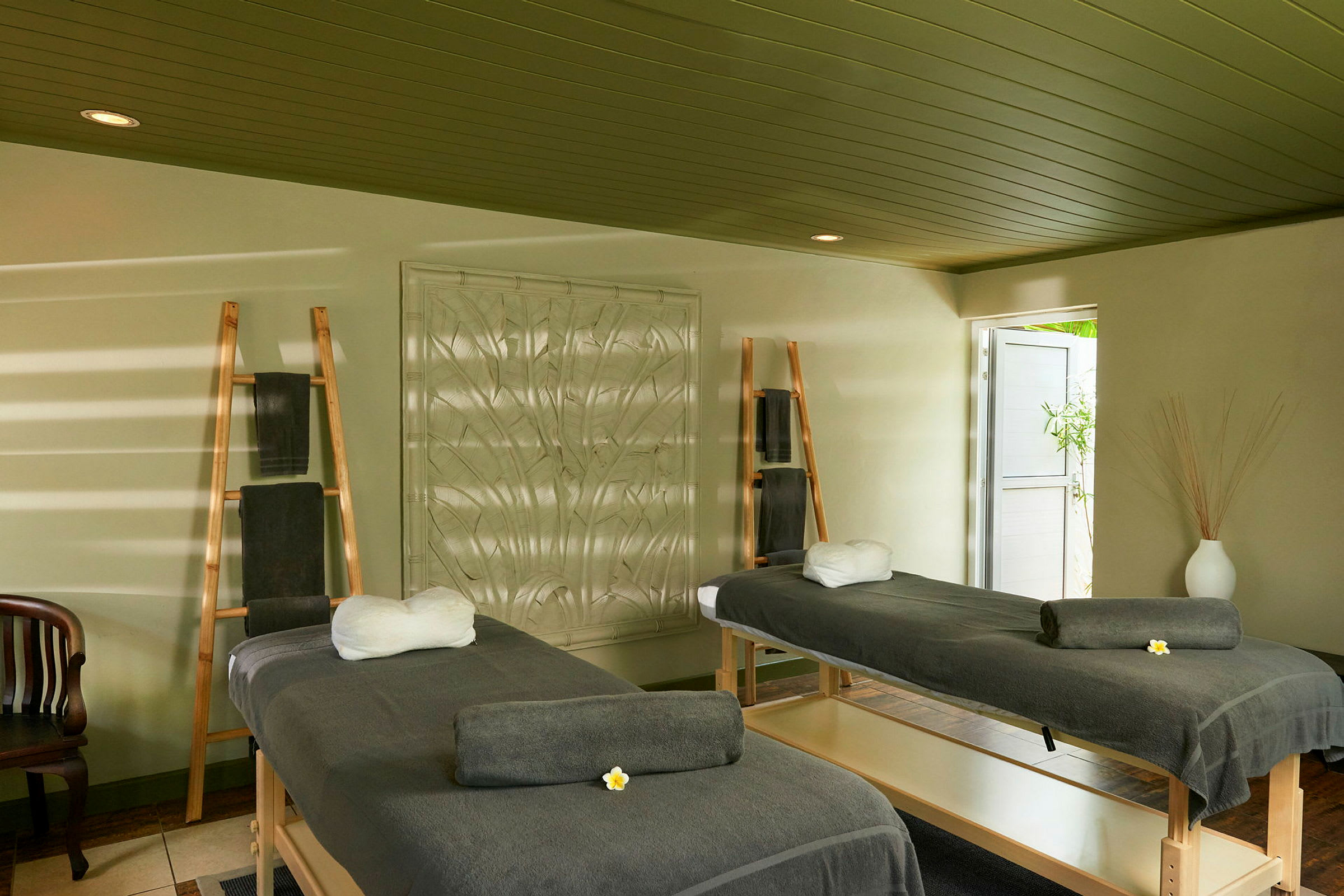 Två massagebänkar med gråa handdukar och vita kuddar i ett rum med rampor och inredning. (AI-genererad text)